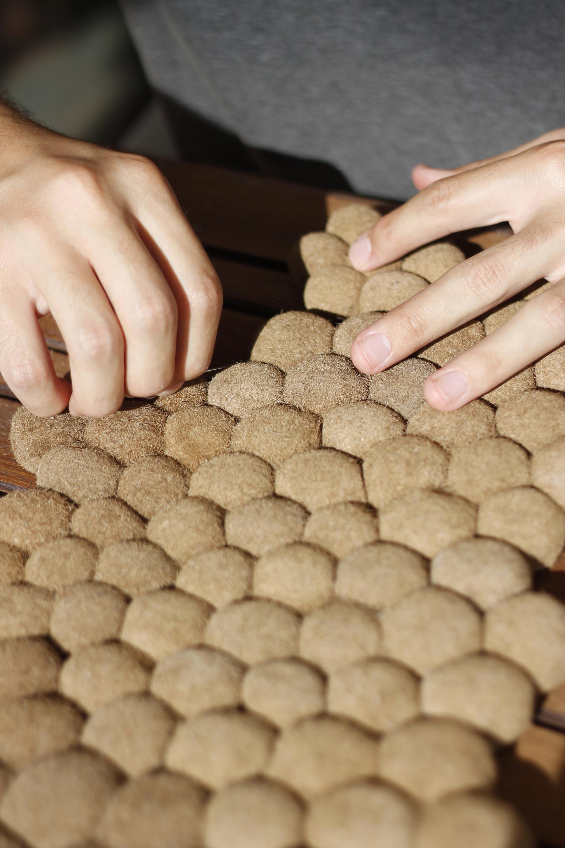 Hands assembling a honeycomb-patterned mat made from repurposed Posidonia seagrass fibers, highlighting sustainable design.