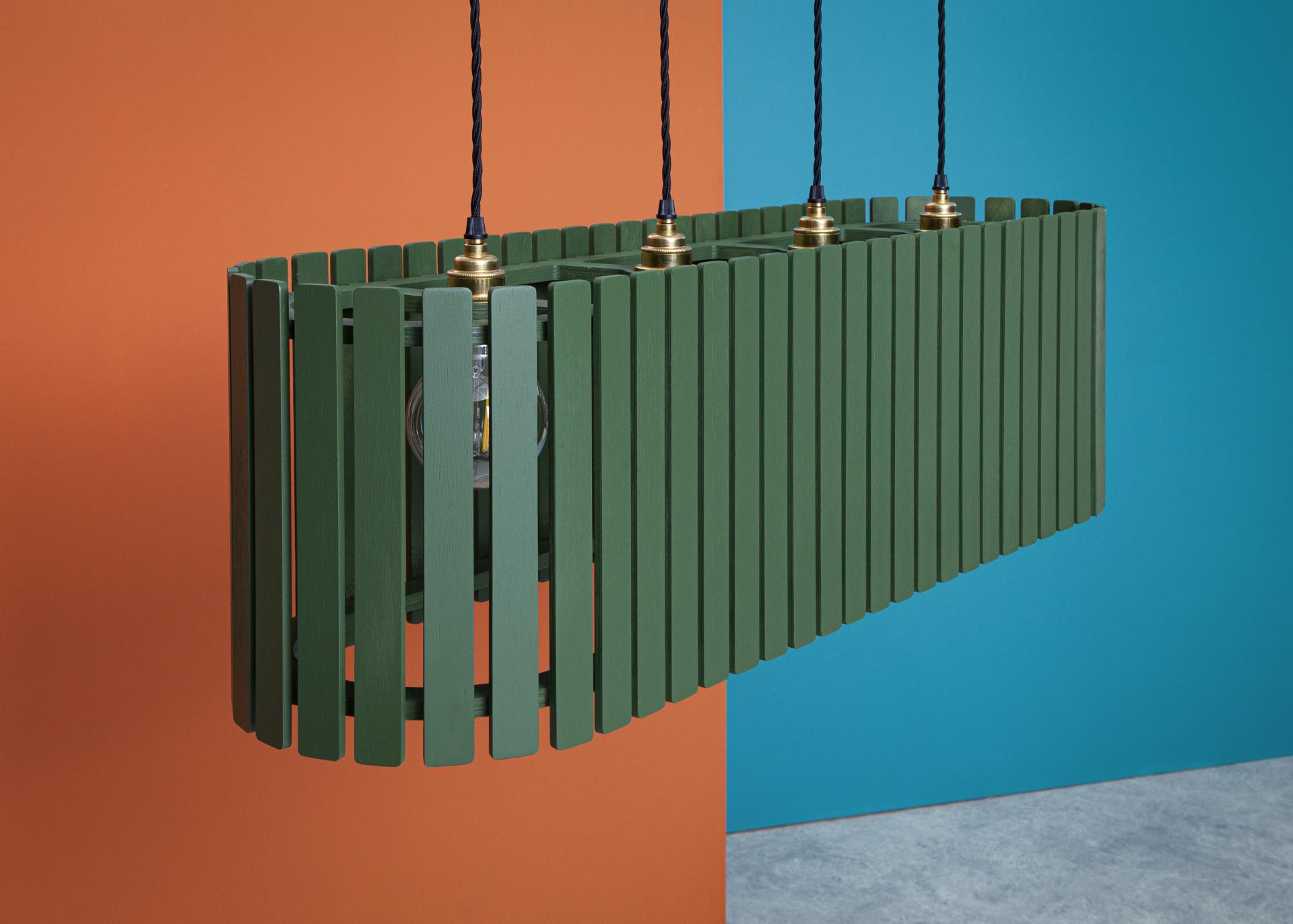 Modern green hanging light fixture against vibrant orange and blue backgrounds, showcasing Liqui Contracts' innovative design at 100% Design.