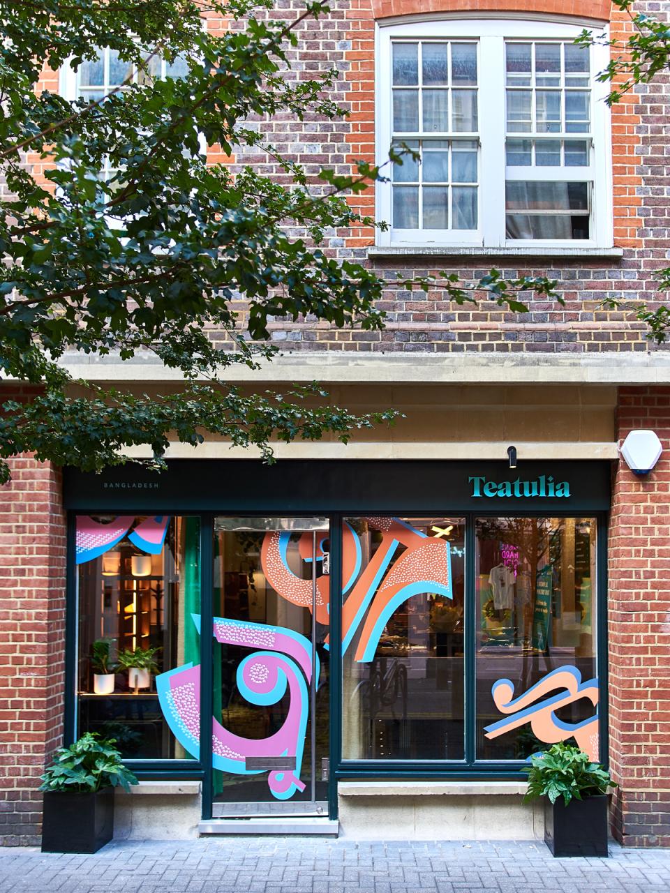 Teatulia's tea shop entrance features vibrant art deco designs and greenery, showcasing stylish interior aesthetics by Russell Sage Studios.