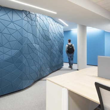 Modern office interior featuring a textured blue wall and a person walking past a desk area.