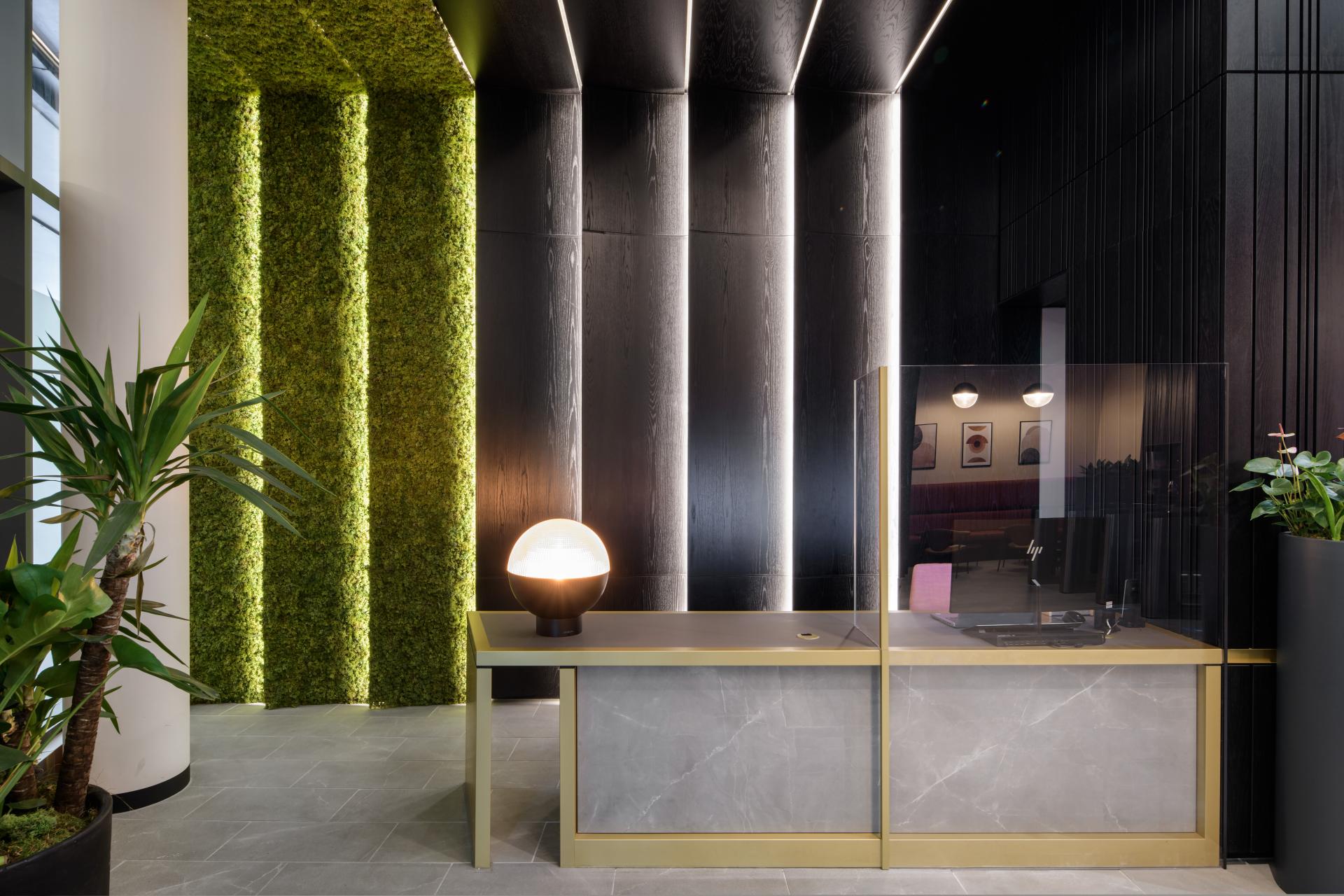 Modern reception area featuring greenery, a sleek desk, and stylish lighting designed by SpaceInvader for One Piccadilly Gardens.