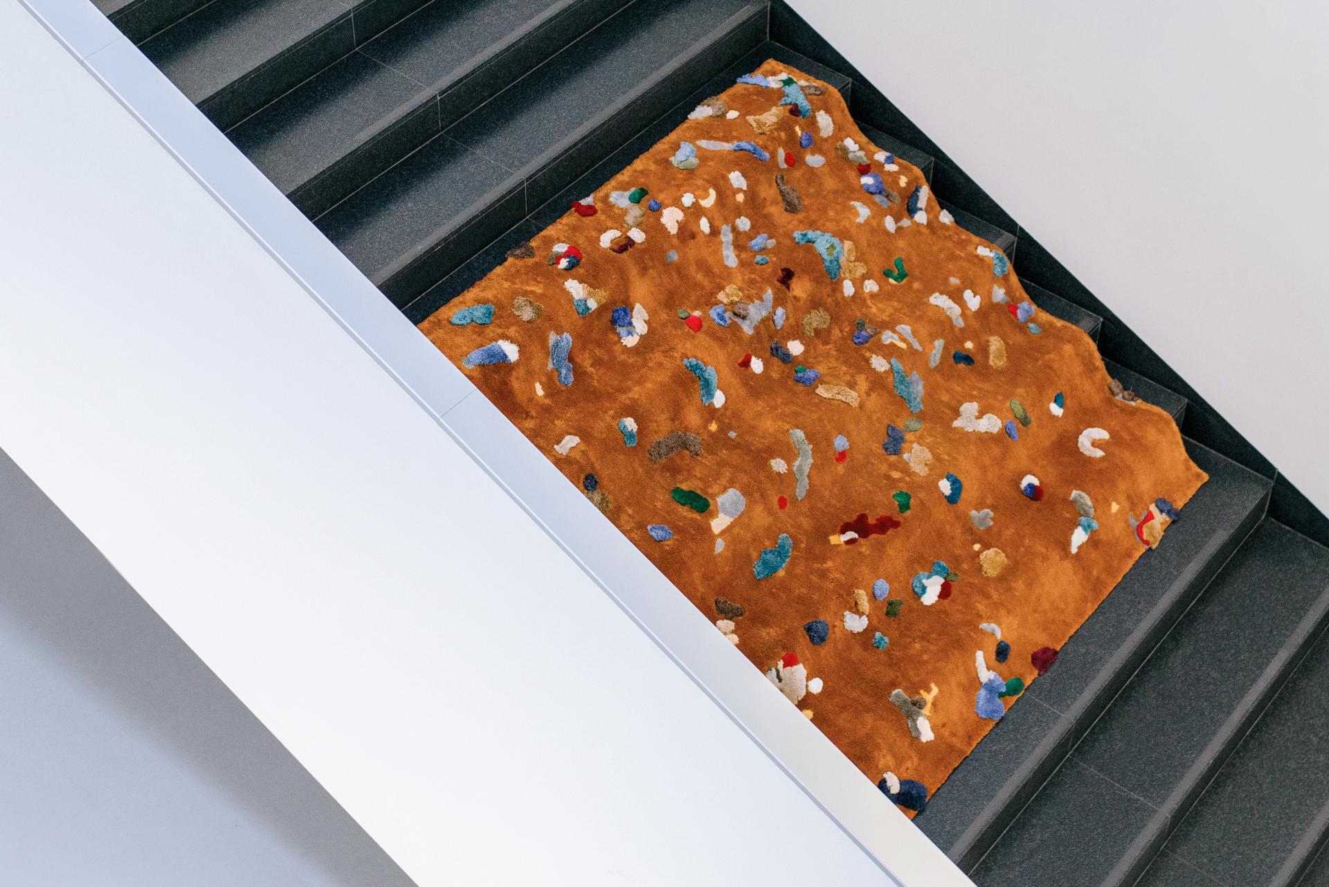 Chaos Rug designed by Audronė Drungilaitė, featuring vibrant colors and unique patterns on a textured orange background.