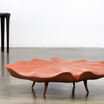 A sculptural coffee table in a petal shape with wooden legs, showcasing innovative furniture design by Christopher Kurtz.