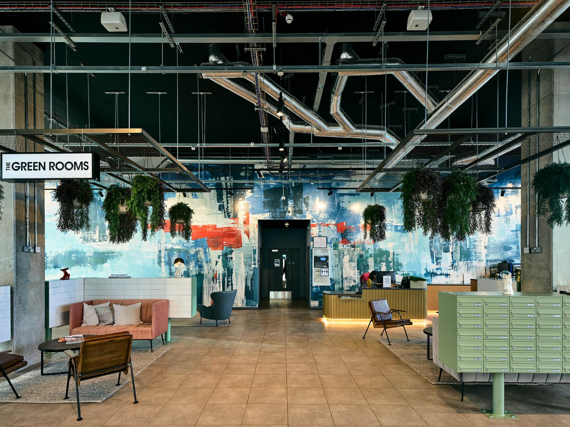 Vibrant interior design of The Green Rooms in Manchester featuring abstract wall art and lush hanging plants, showcasing modern architecture.