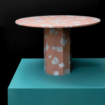 Circular terrazzo table with a pink surface and marble accents, set on a teal base, showcasing modern design elements.
