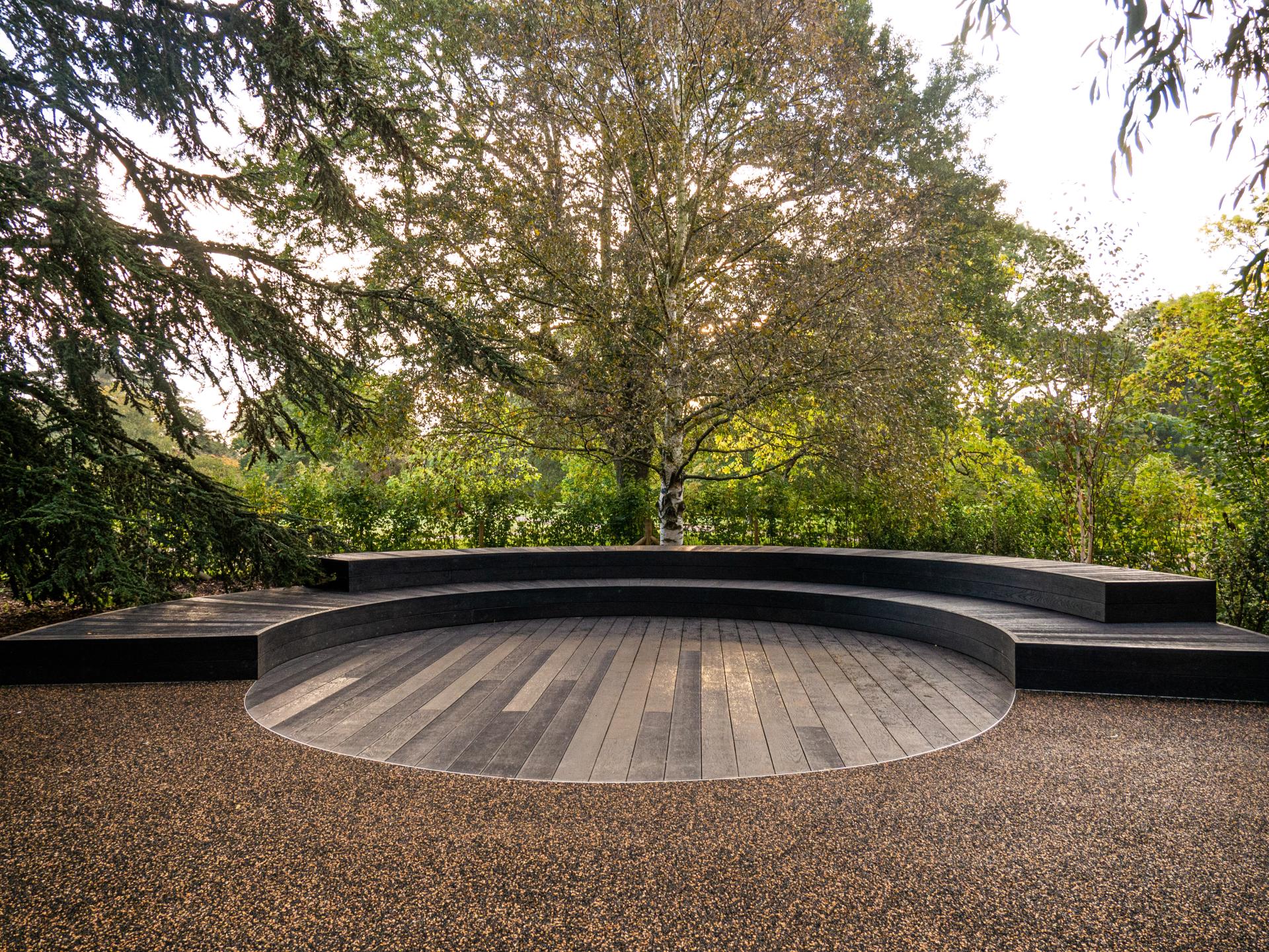 Contemporary outdoor seating area with layered wooden platforms and surrounding greenery at Kew Gardens.