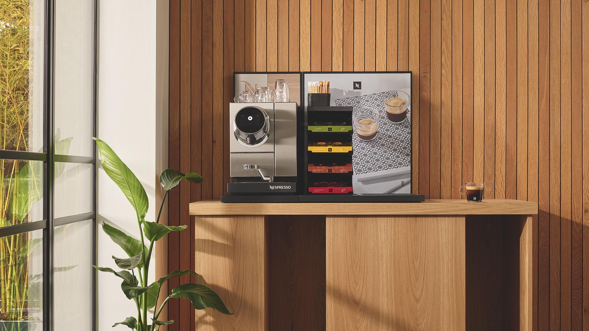 Modern coffee station with Nespresso machine, colorful capsule storage, and glassware against a wooden backdrop.