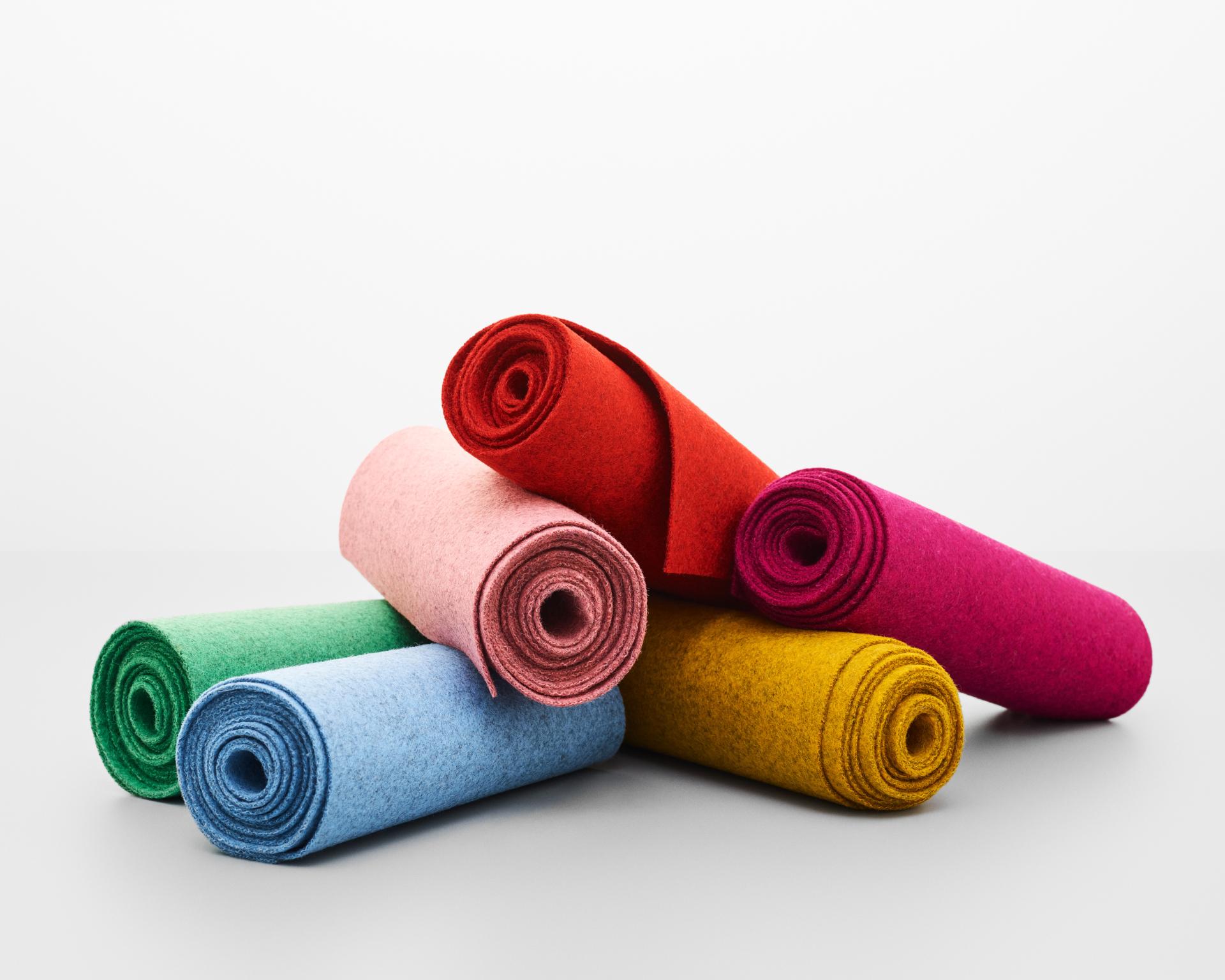 Colorful rolled fabrics from Kvadrat's Divina Melange range, showcasing a vibrant palette of blues, pinks, greens, and yellows.