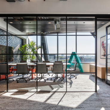 Modern office space featuring a glass conference room with stylish furniture, greenery, and a vibrant design for Alpha FX London.