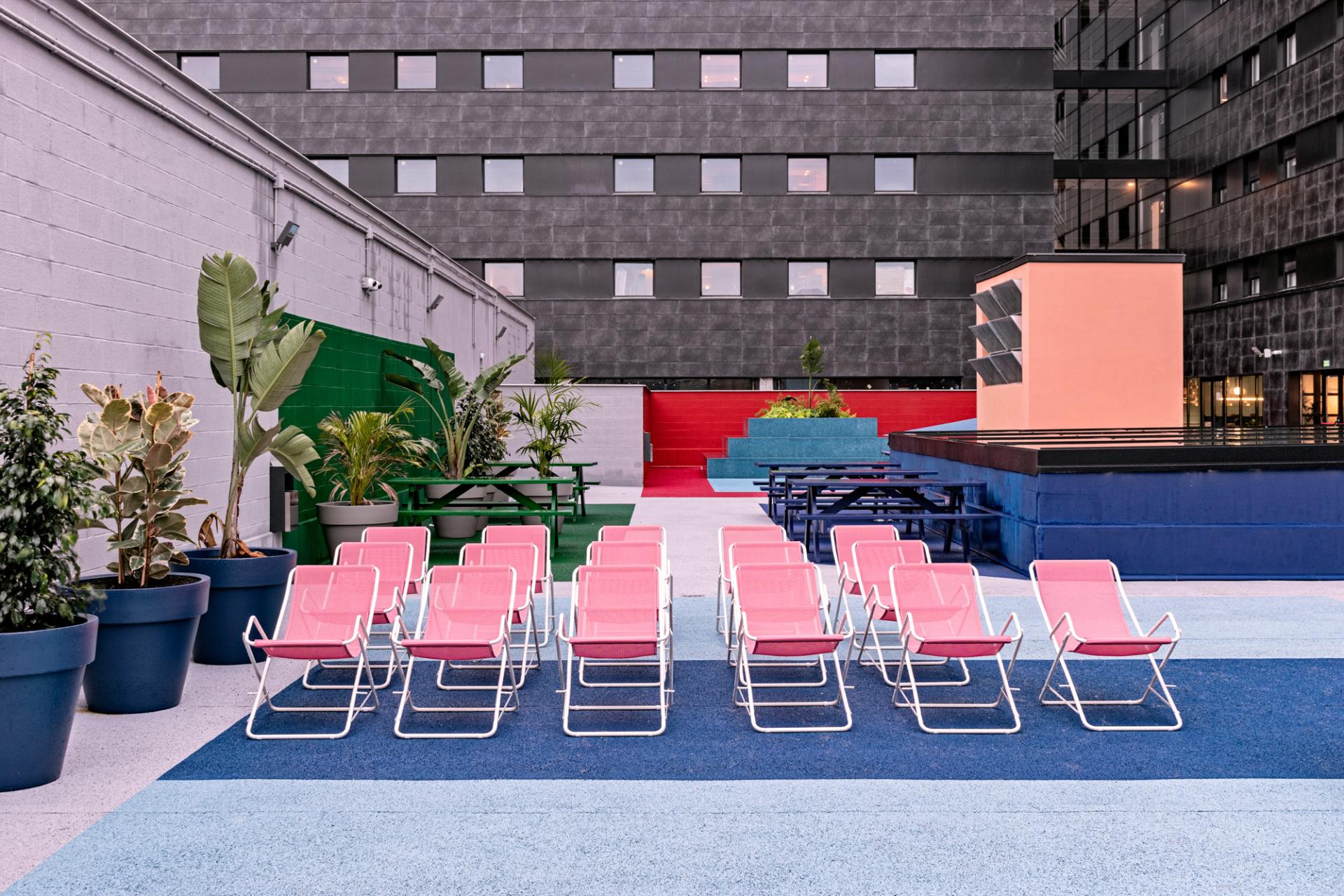 Colorful outdoor seating area with pink chairs and vibrant landscaping at the University Residence Resa San Mamés in Bilbao.