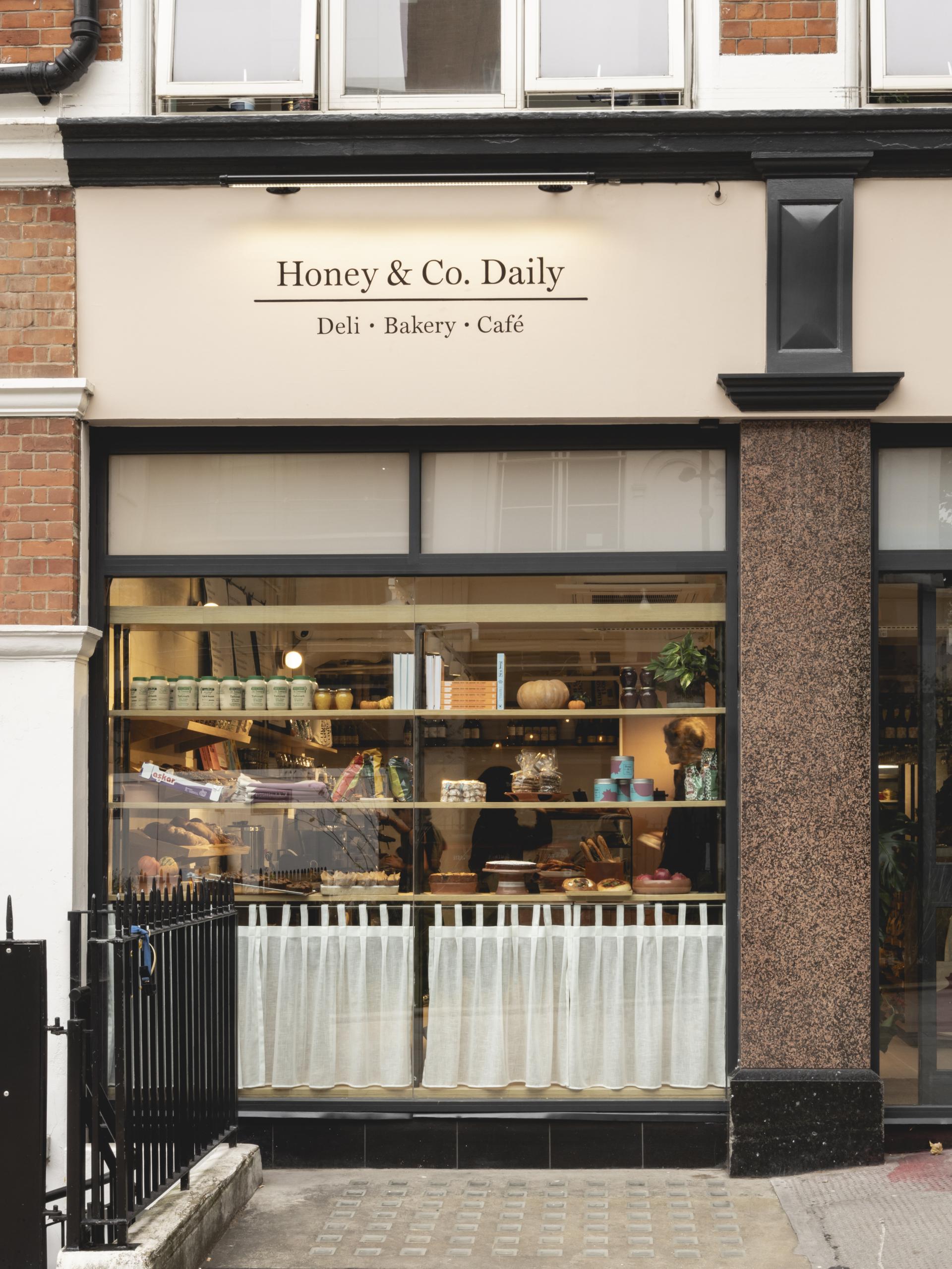 Exterior view of Honey & Co. Daily, showcasing the deli, bakery, and café with inviting displays and rich textures.