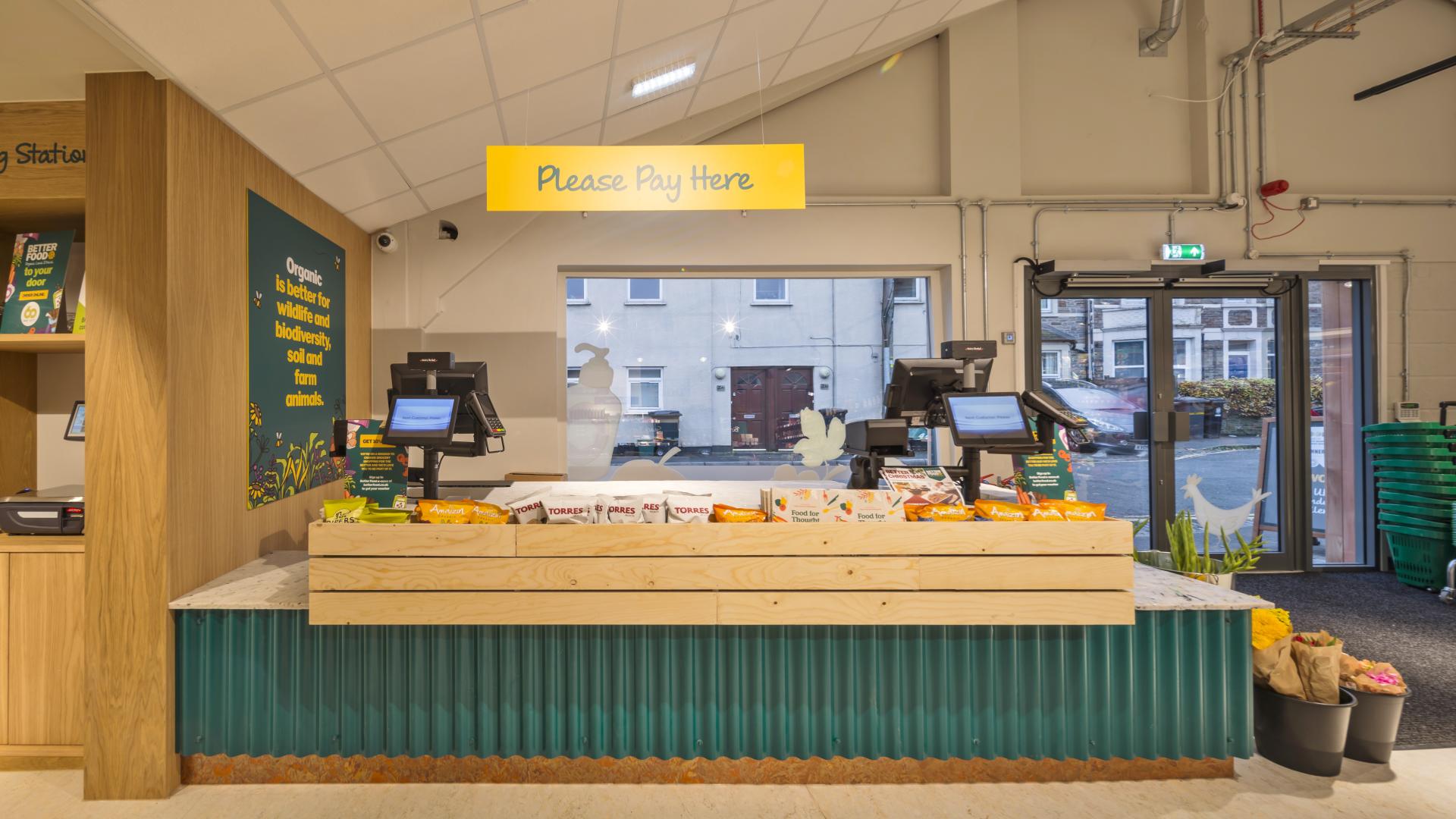 Brightly designed checkout area at Better Food's new Gloucester Road store, featuring organic products and modern payment stations.