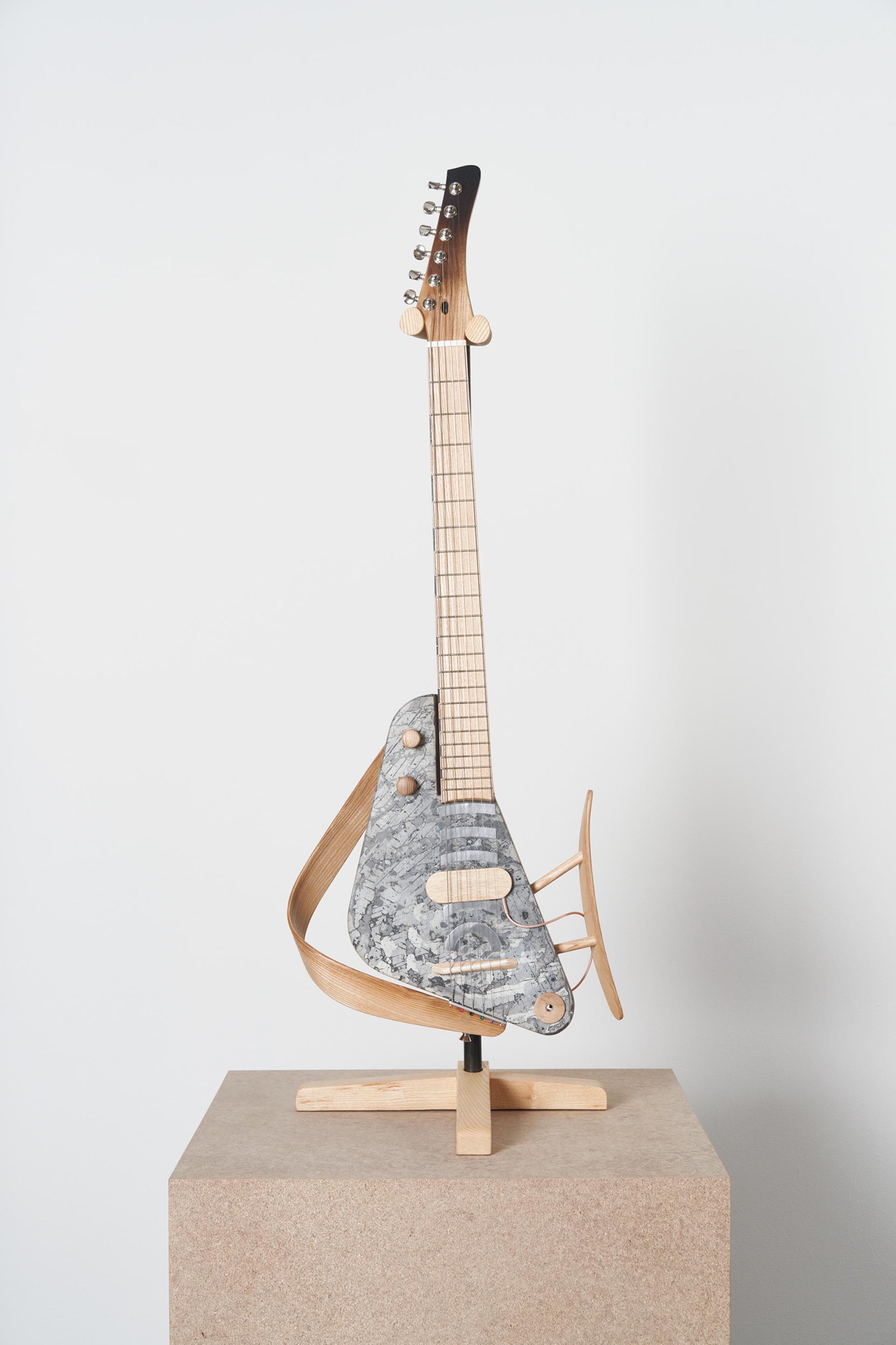 Innovative ash tree guitar sculpture displayed on a pedestal, showcasing Scotland's craftsmanship and environmental artistry.