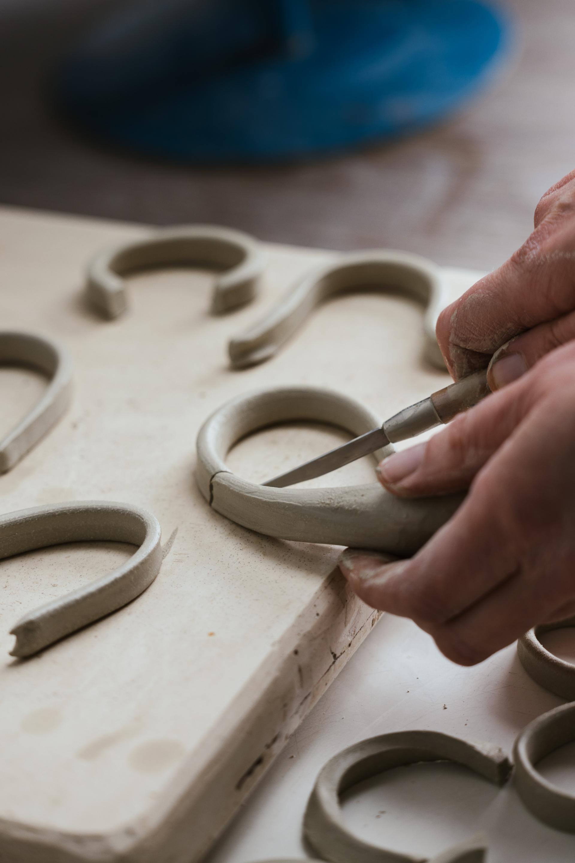 Craftsperson shaping clay ceramic pieces with a knife, highlighting the delicate artistry of ceramics at Harewood House Biennial.