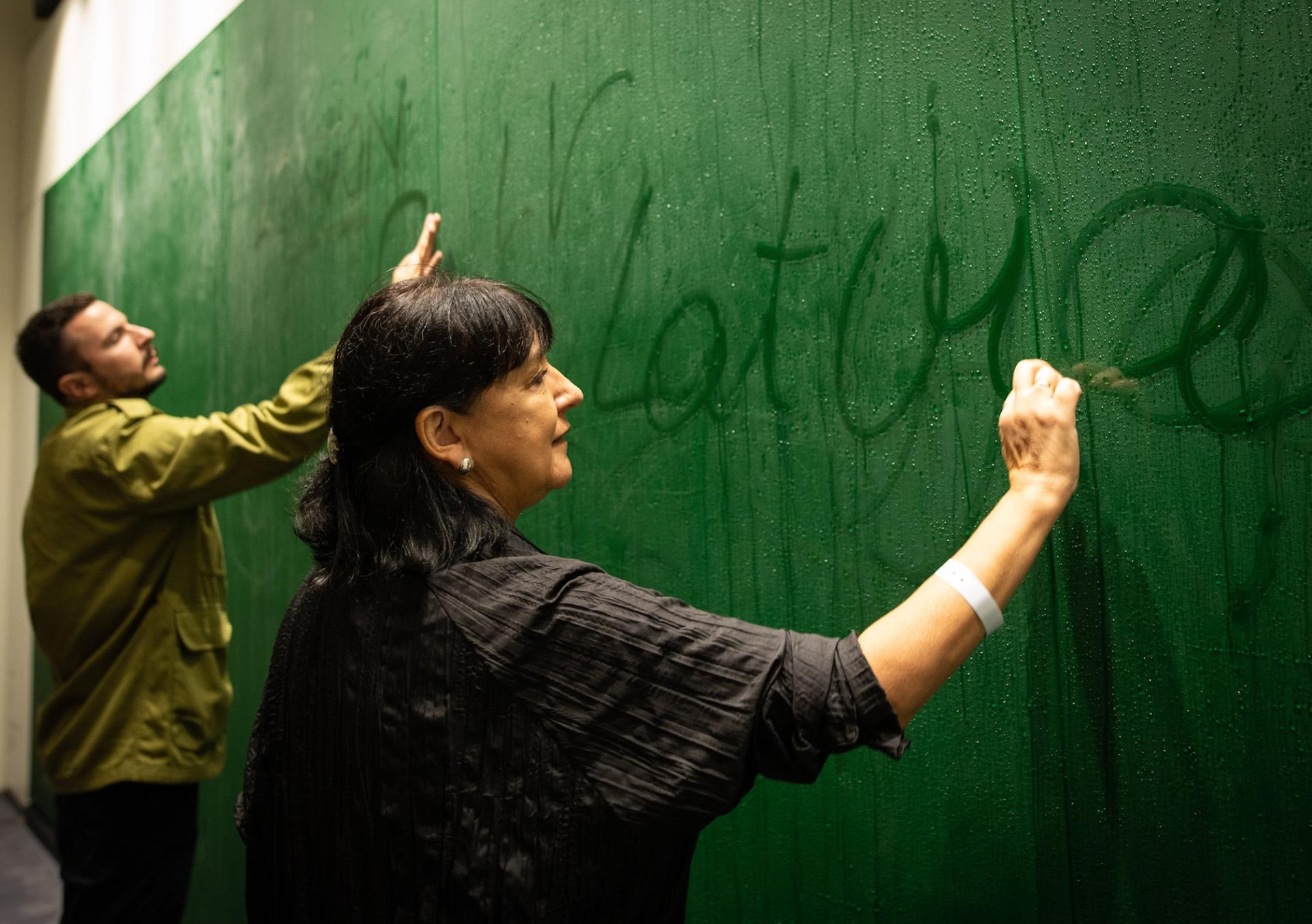 Artists interacting with a green wall installation at the London Design Biennale, showcasing creative engagement in design.