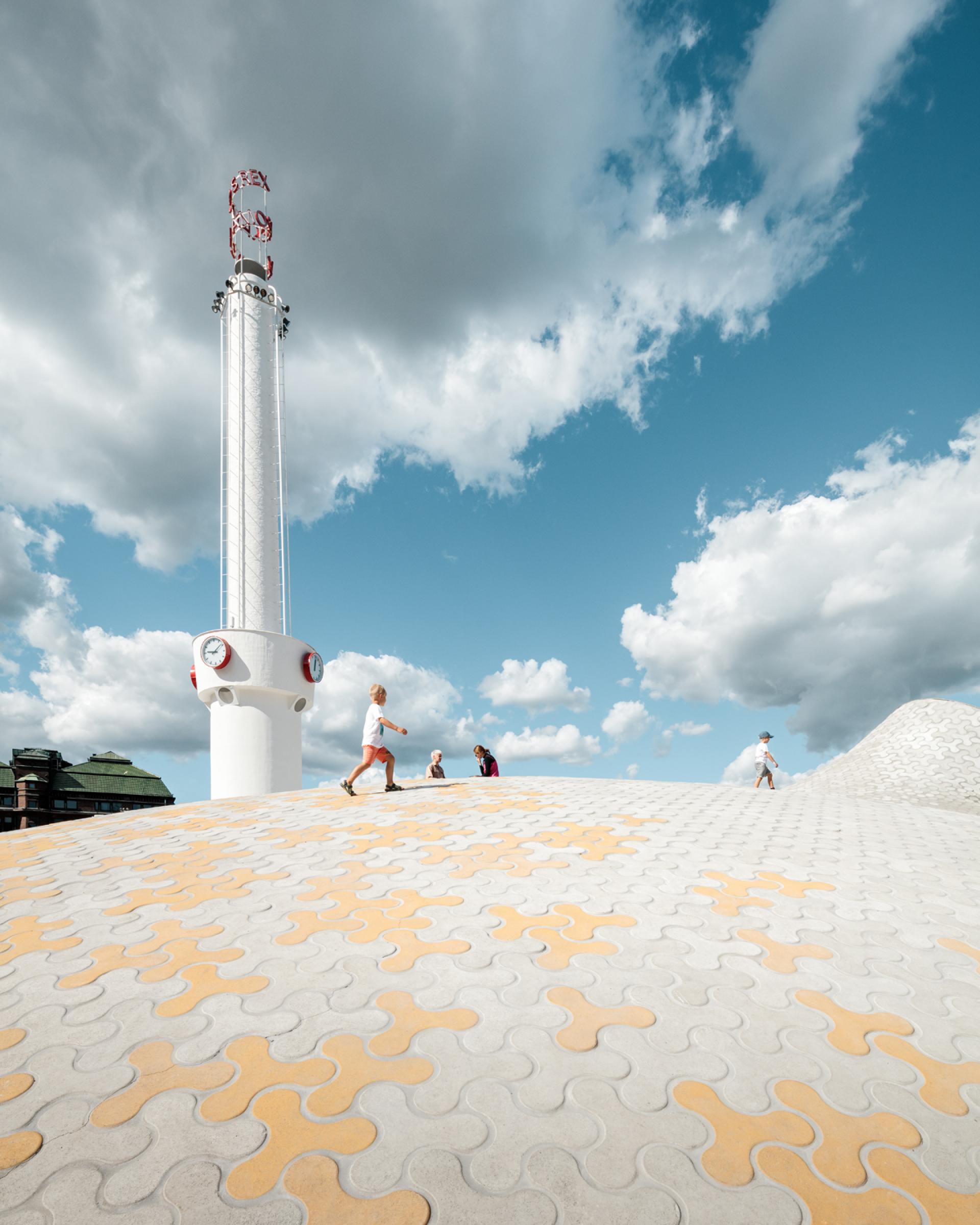 Visitors explore the unique patterned rooftop of Helsinki's new art museum under a blue sky with clouds.