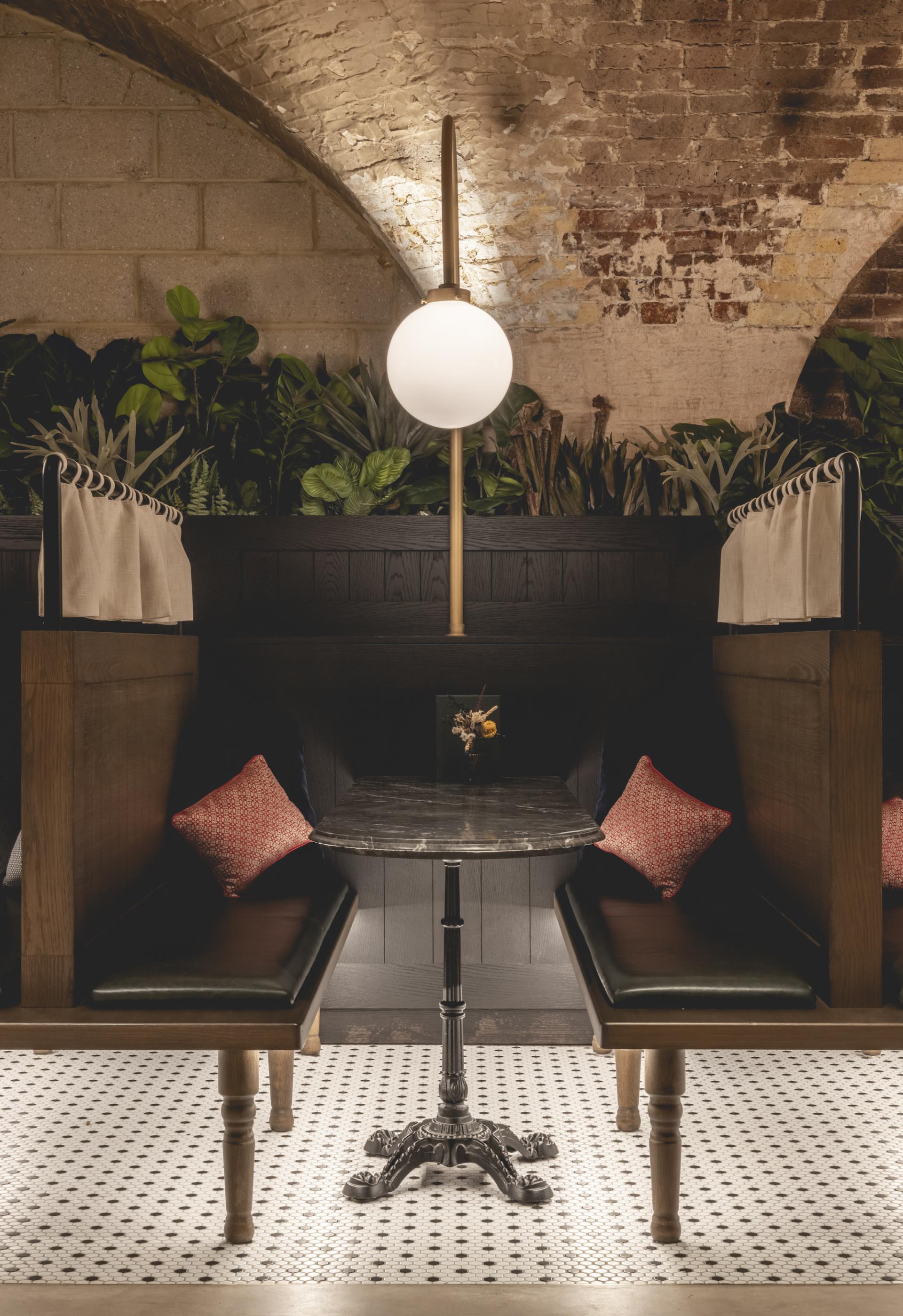 Stylish seating area at The Libertine, featuring elegant lighting, lush plants, and vintage-inspired decor.