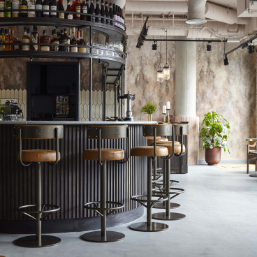 Stylish bar area of Kricket restaurant, featuring modern stools, a drink display, and a warm, inviting atmosphere.
