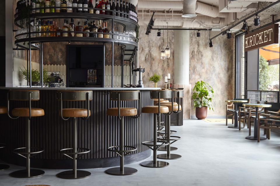 Stylish bar area of Kricket restaurant, featuring modern stools, a drink display, and a warm, inviting atmosphere.