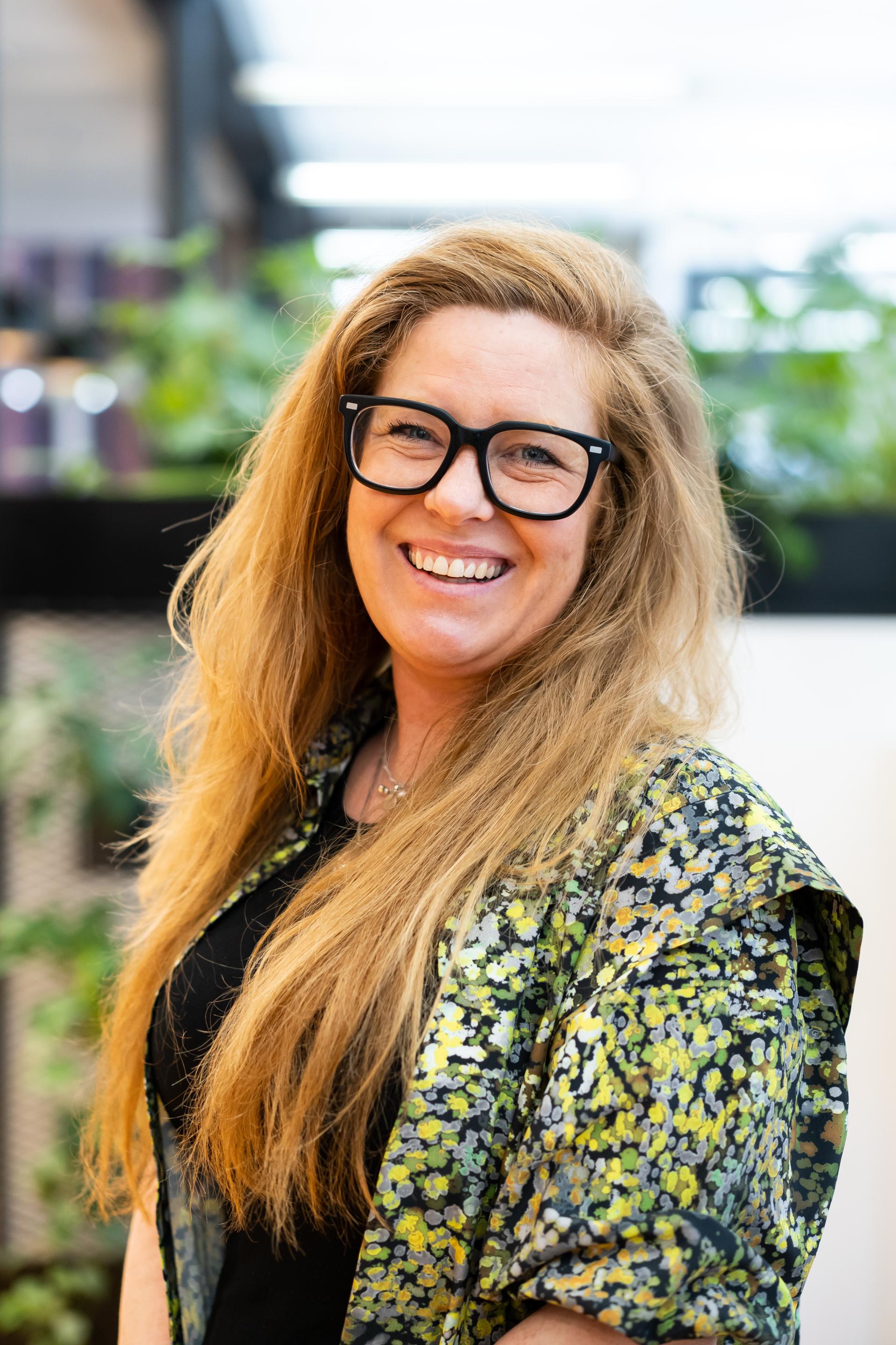 Smiling woman in a floral jacket, highlighting sustainable design and community engagement in the built environment.