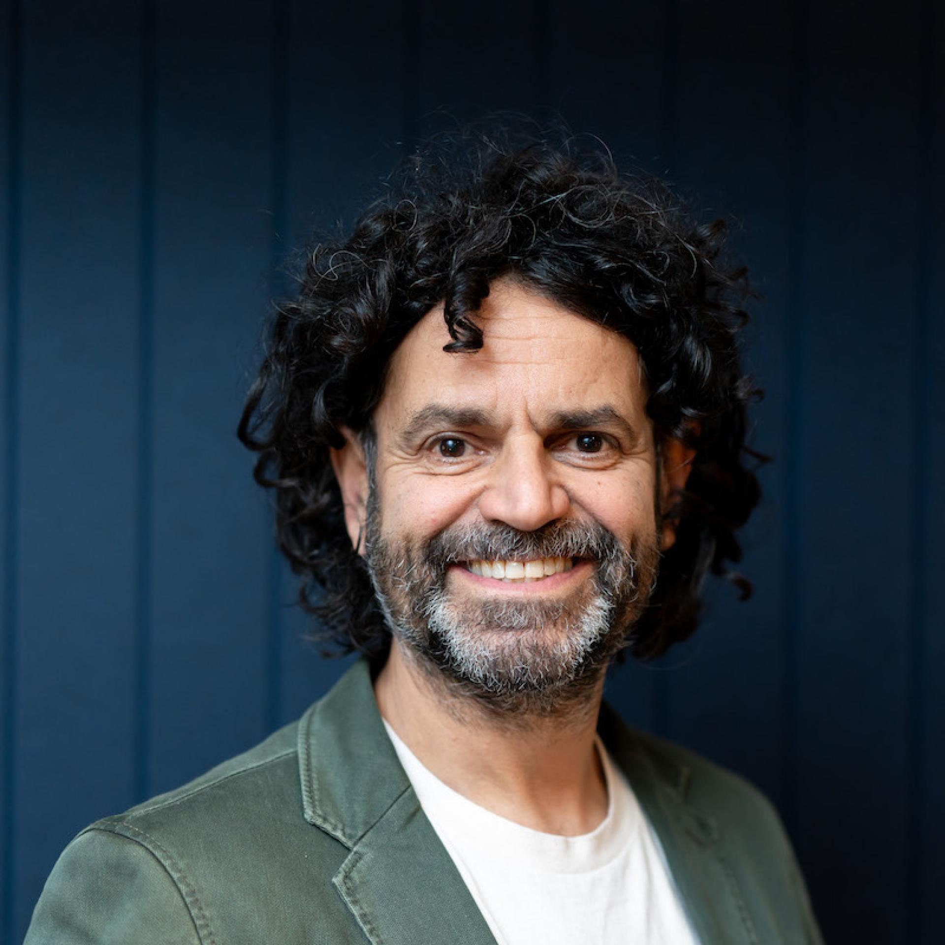 Smiling man with curly hair in a casual blazer, representing modern workplace dynamics and professionalism.