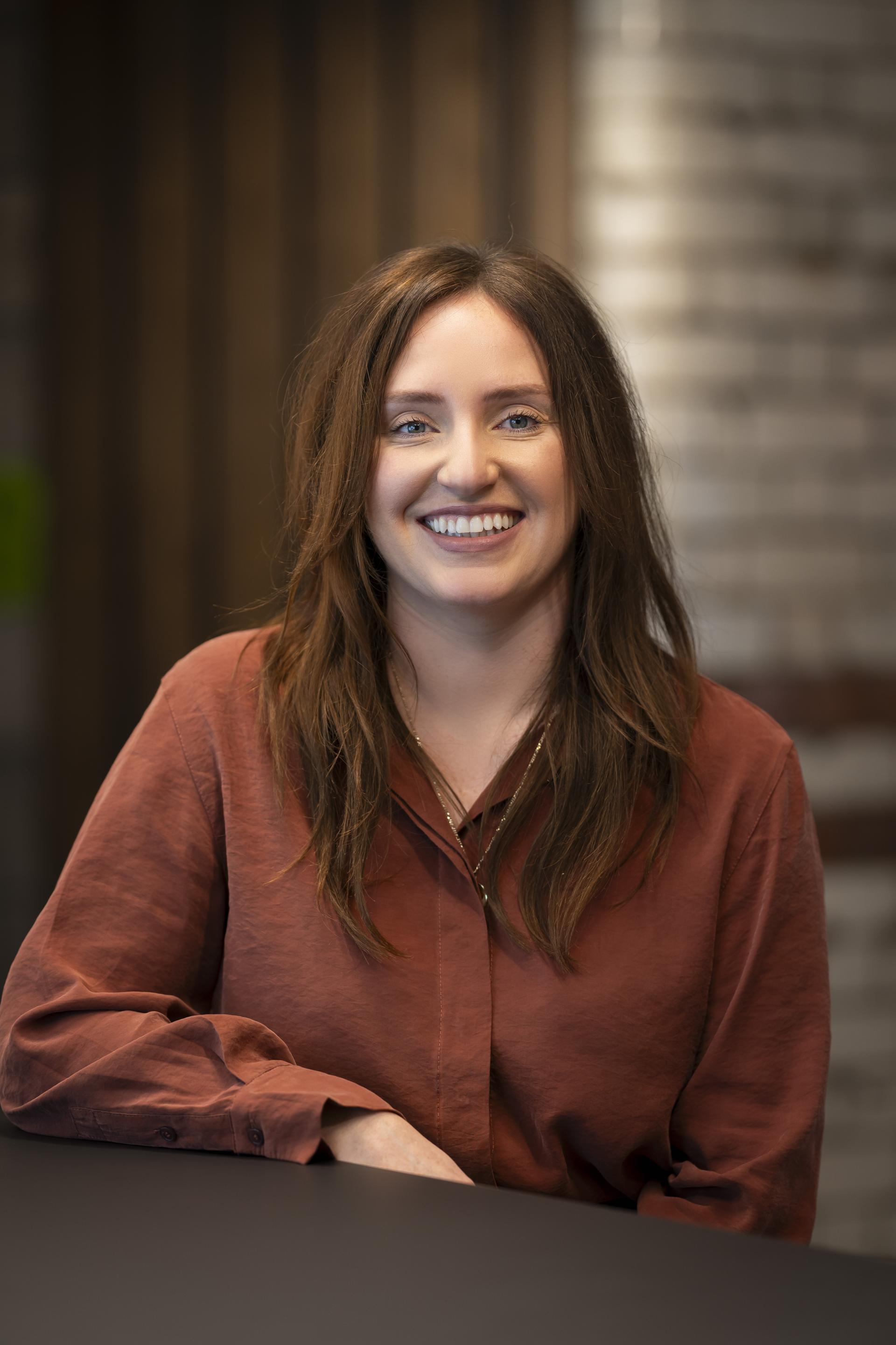 Smiling woman in a rust-colored shirt, discussing technology's role in sustainable design in an office setting.