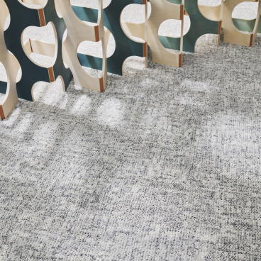Textured gray carpet from Ege's ReForm Memory collection, featuring a modern wooden partition emphasizing human-centered design.