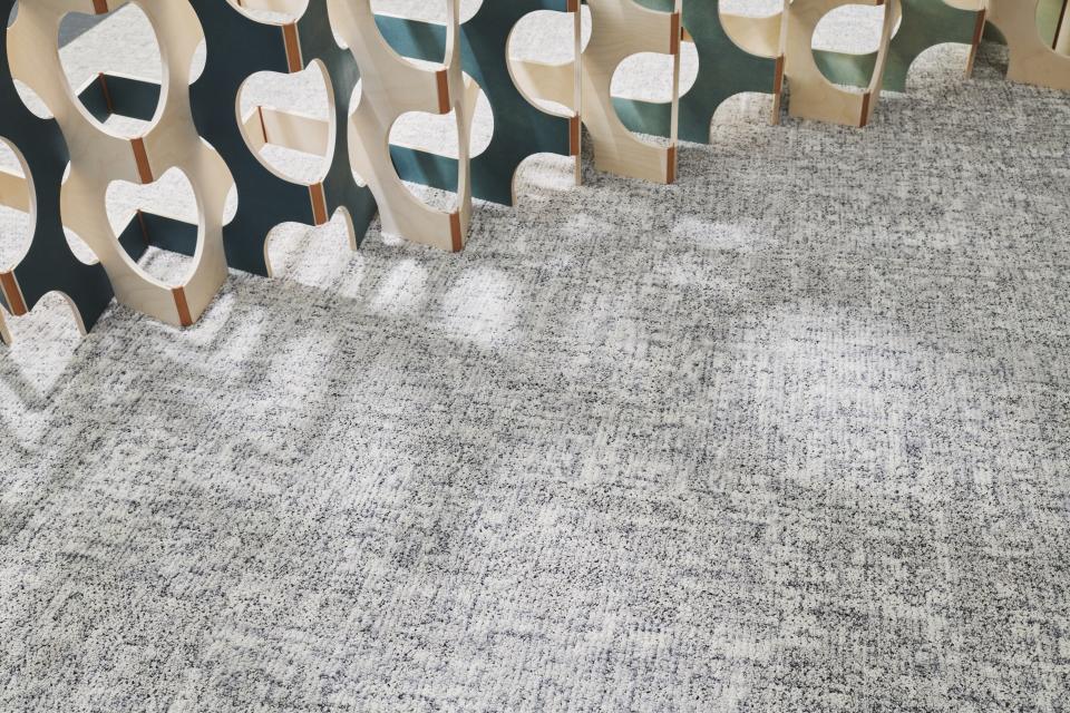 Textured gray carpet from Ege's ReForm Memory collection, featuring a modern wooden partition emphasizing human-centered design.
