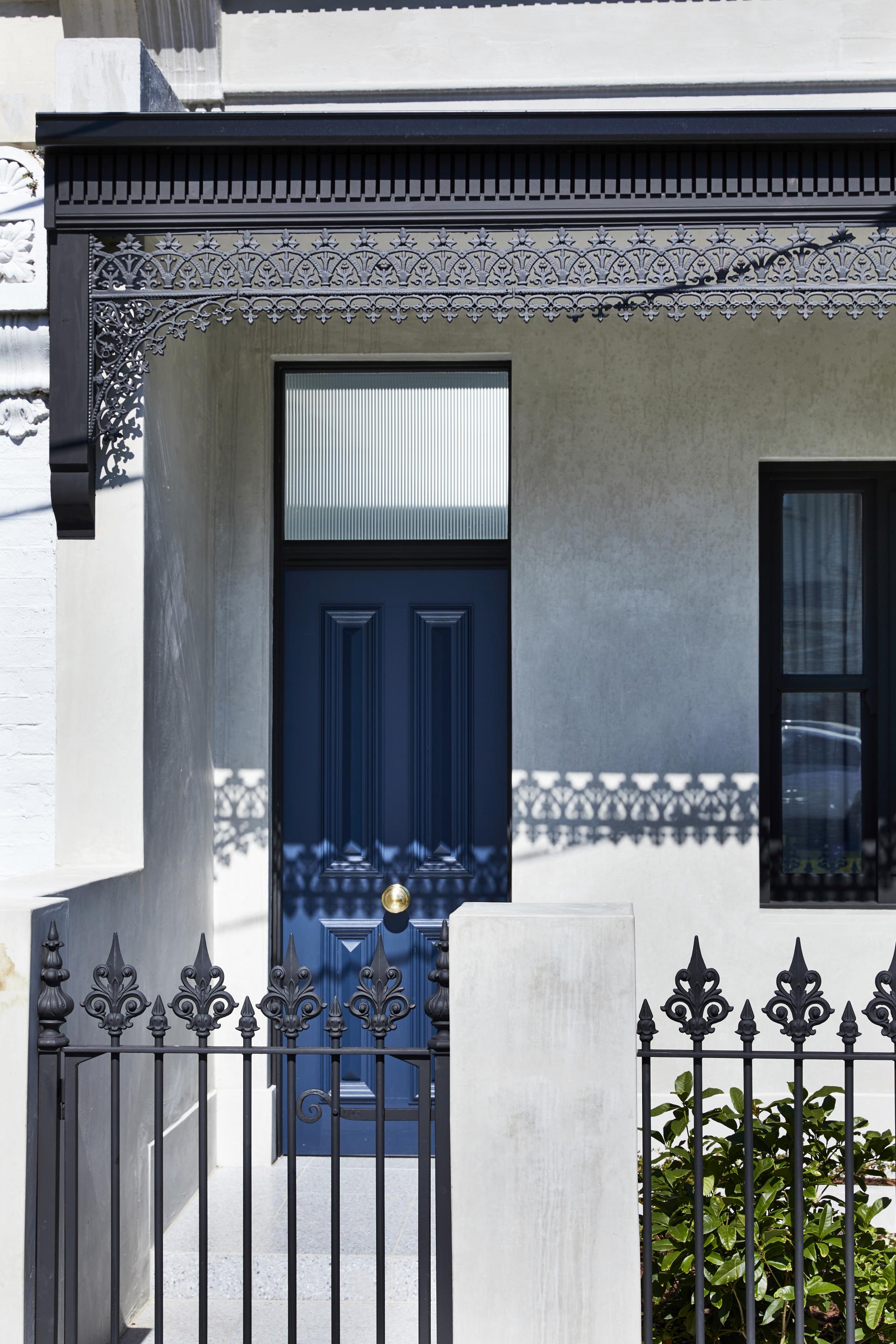 Elegant Melbourne home entrance featuring a blue door, decorative ironwork, and lush greenery inspired by Parisian design.