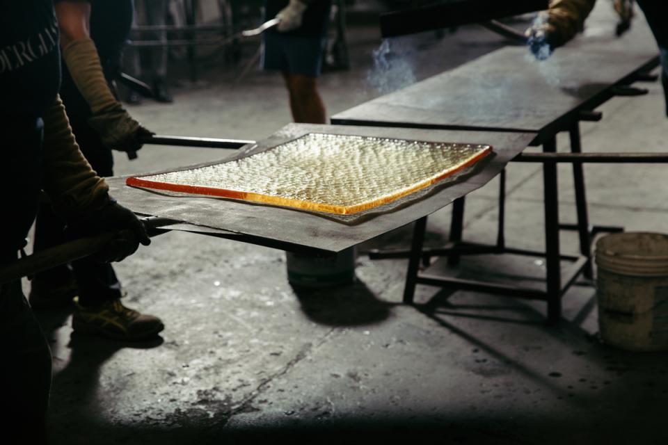 Artisans handle a glowing, cast glass sheet, showcasing the craftsmanship behind WonderGlass and nendo's Melt furniture collection.