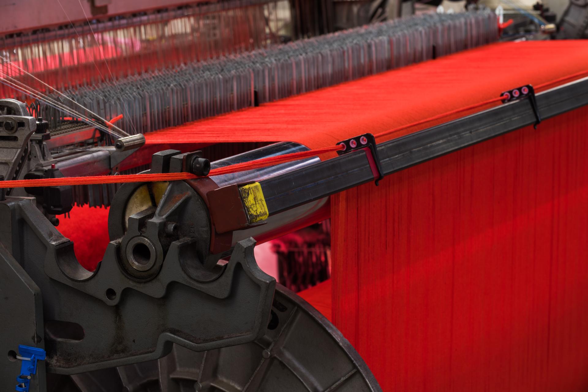 Textile manufacturing machinery in a mill, showcasing vibrant red fabric production and the intricacies of weaving technology.