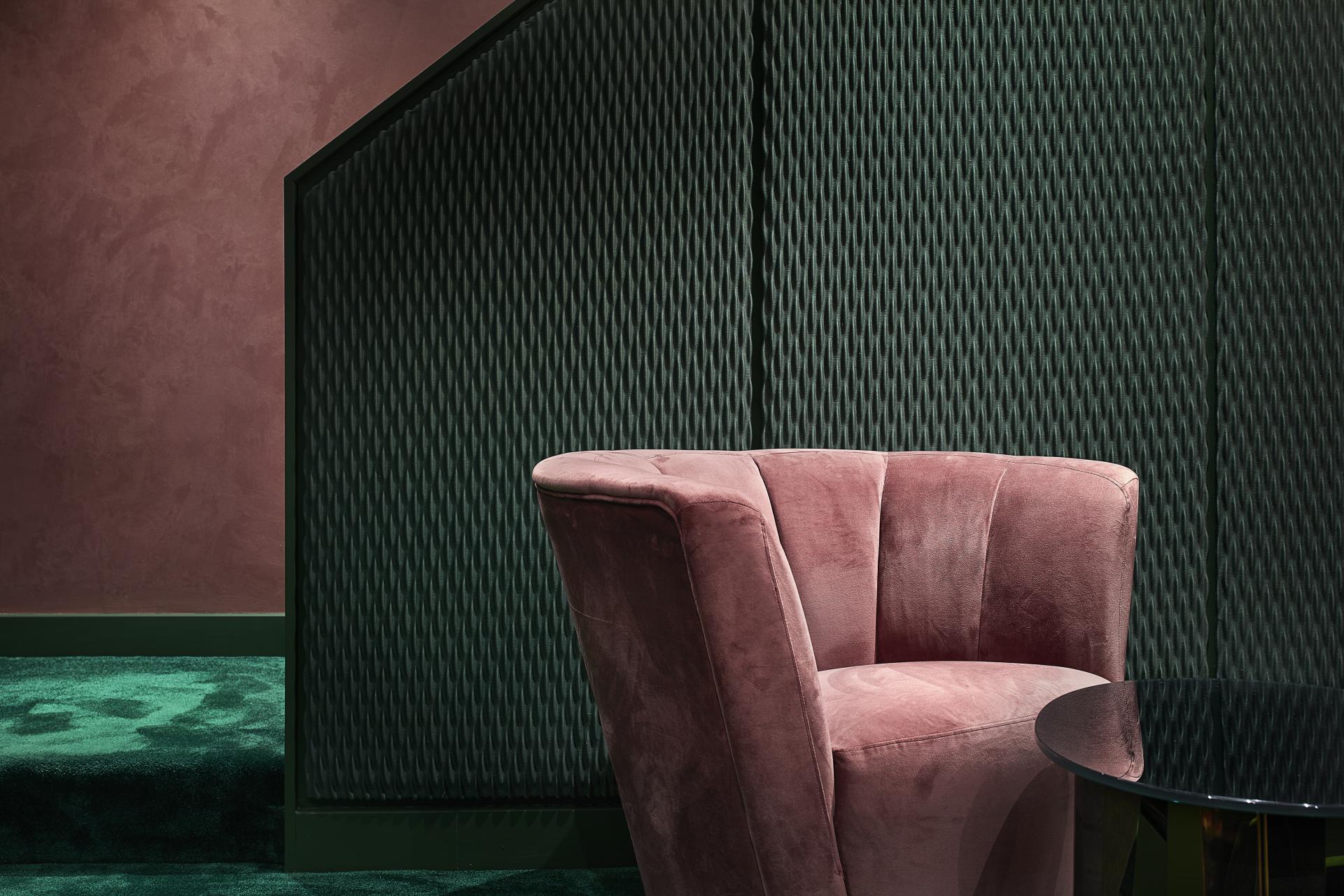 Stylish pink velvet chair beside a sleek black table against a textured green wall in Bluebells Restaurant.