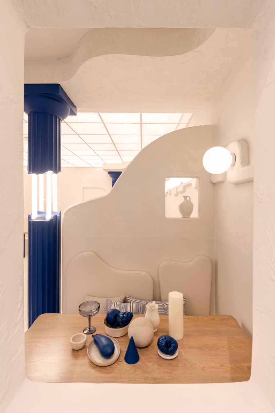 Contemporary Greek restaurant interior featuring blue and white decor, sculptural tableware, and cozy seating for diners.