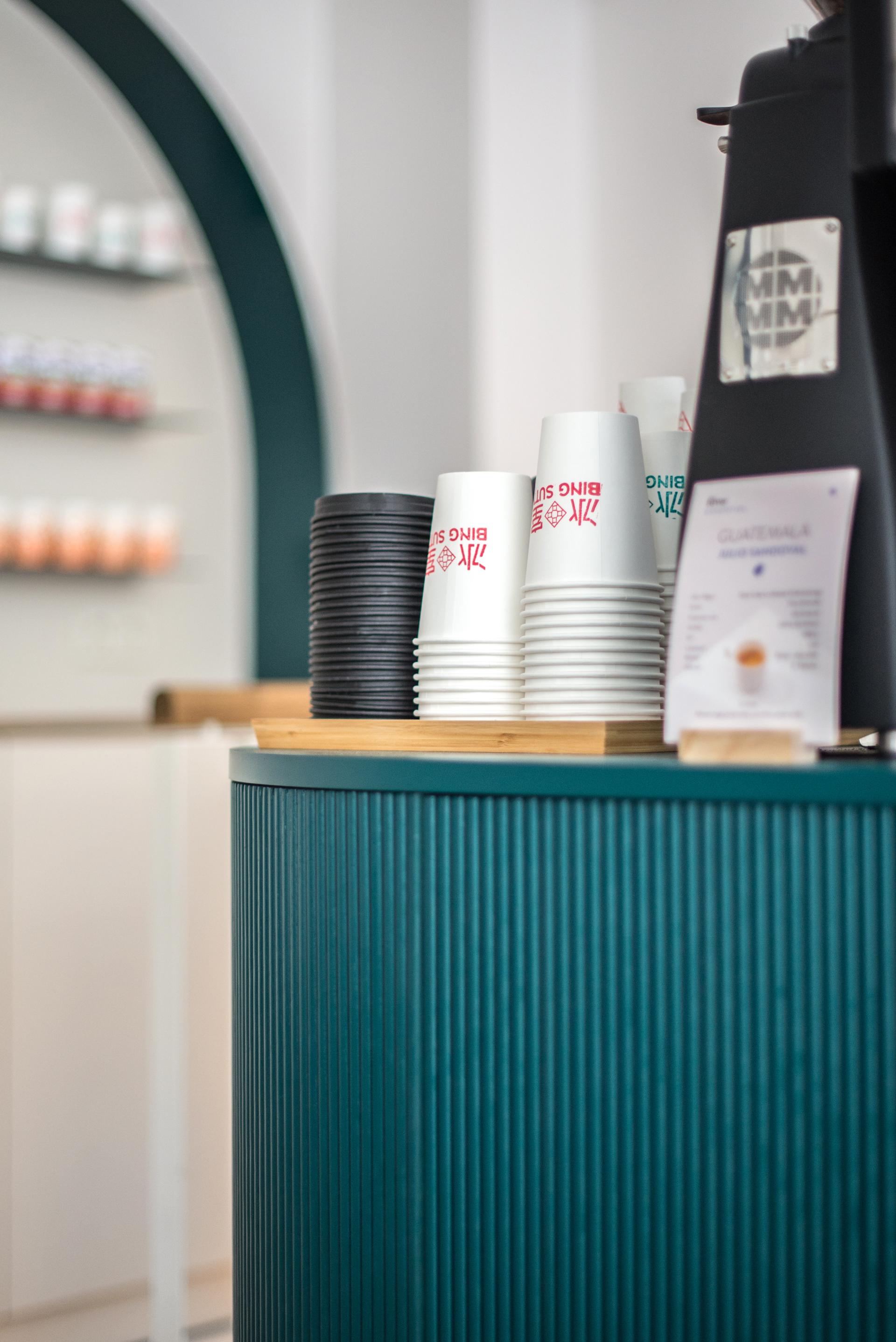 Modern Hong Kong Bing Sutt café interior featuring stacked cups and a teal counter at HOP Architects' Paris location.