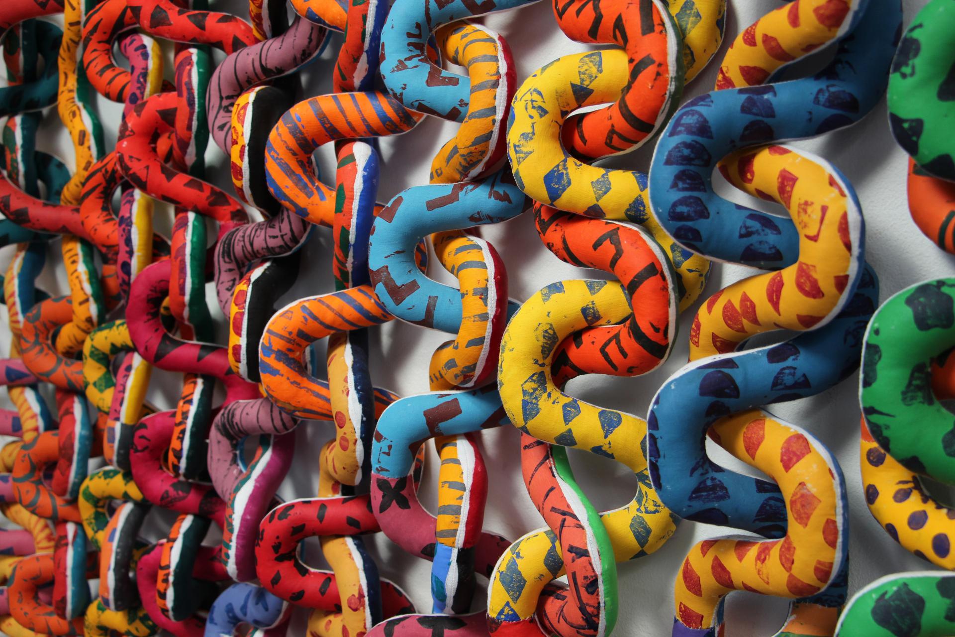 Colorful textile art installation featuring interconnected fabric chains, showcasing British textile artist Anna Ray's tribute to London's weaving history.