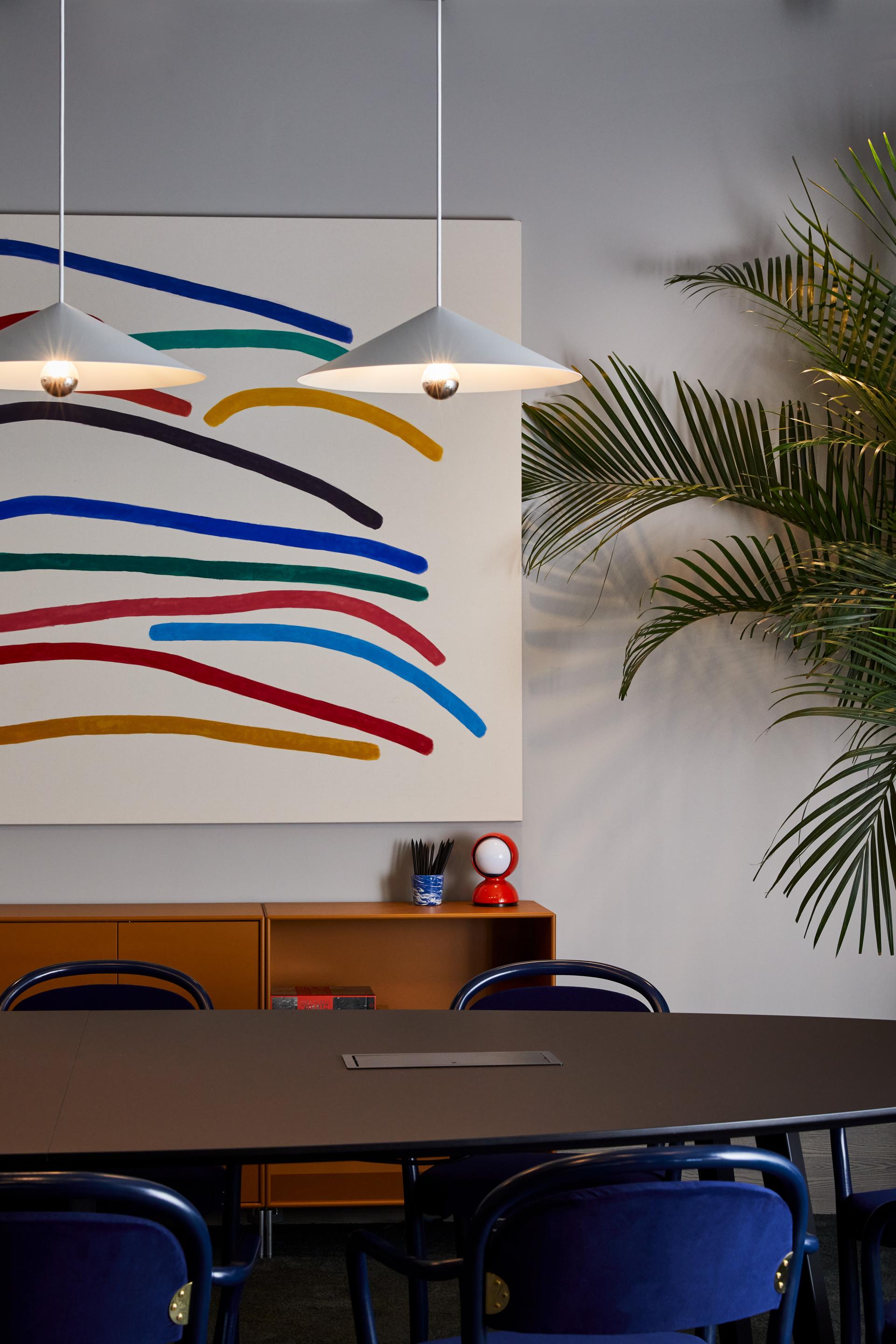 Modern conference room in The Office Group's Notting Hill workspace, featuring vibrant artwork, stylish lighting, and tropical plants.