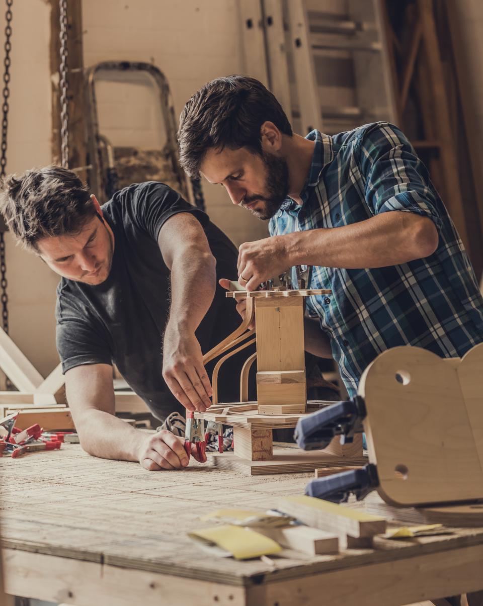 Two craftsmen collaborate on designing bespoke lampshades in a workshop, inspired by art deco elements.