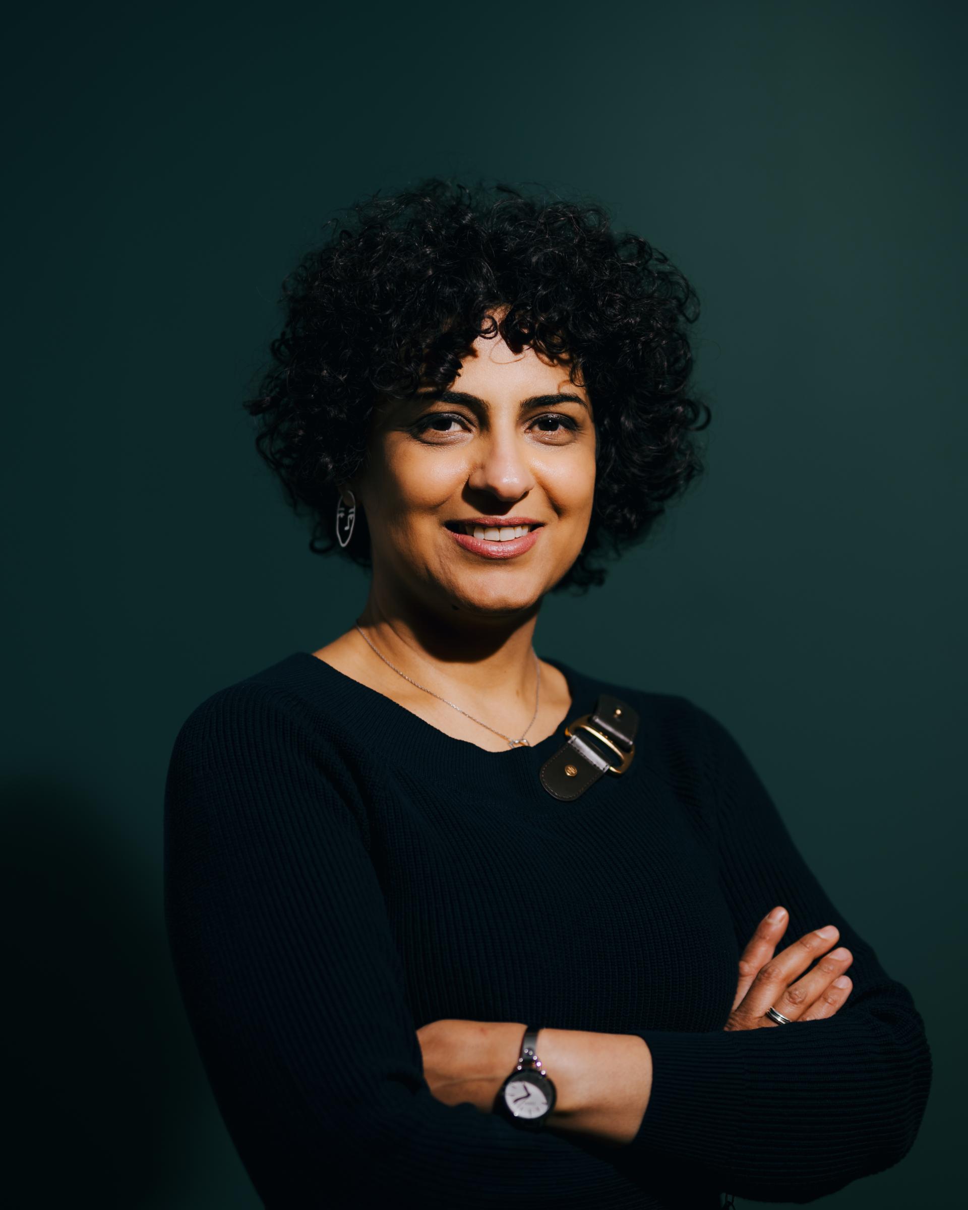 Smiling woman with curly hair, wearing a black sweater, discusses neurodiversity at Material Source Studio in Glasgow.
