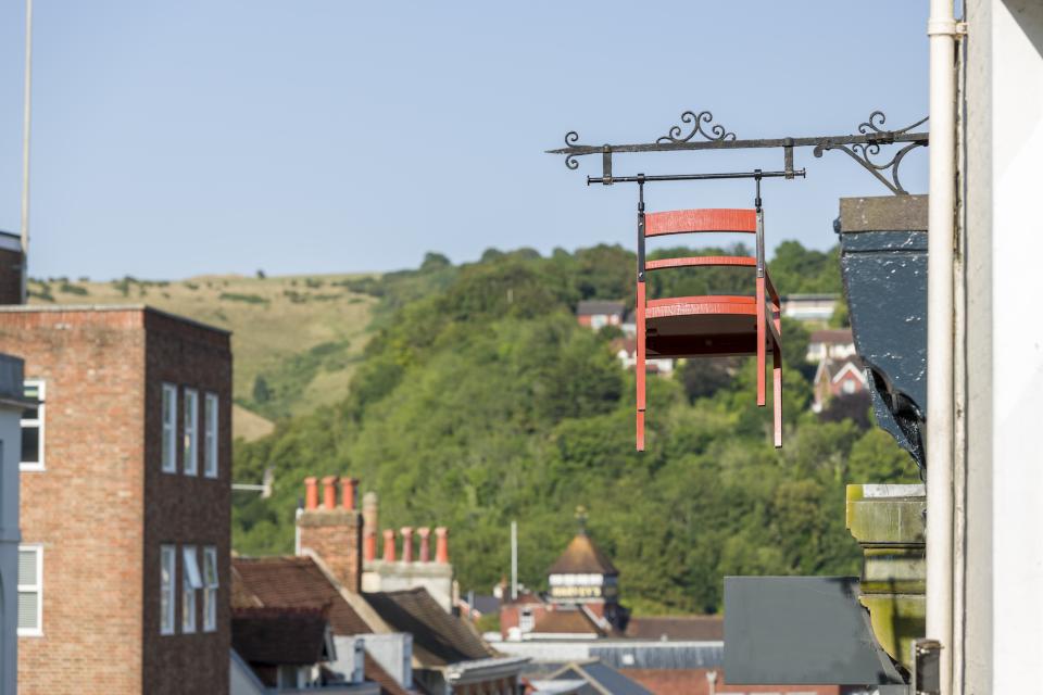 A vibrant red chair hangs from an ornate bracket above Lewes, showcasing innovative retail design by An Actual Kitchen.