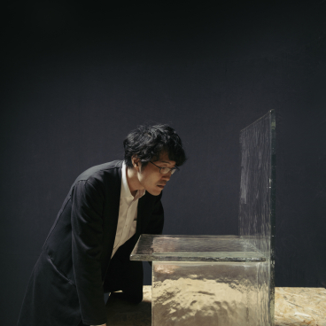 Designer intently examines Melt, a delicate, cast glass table that appears to float, showcasing innovative furniture design by nendo and WonderGlass.