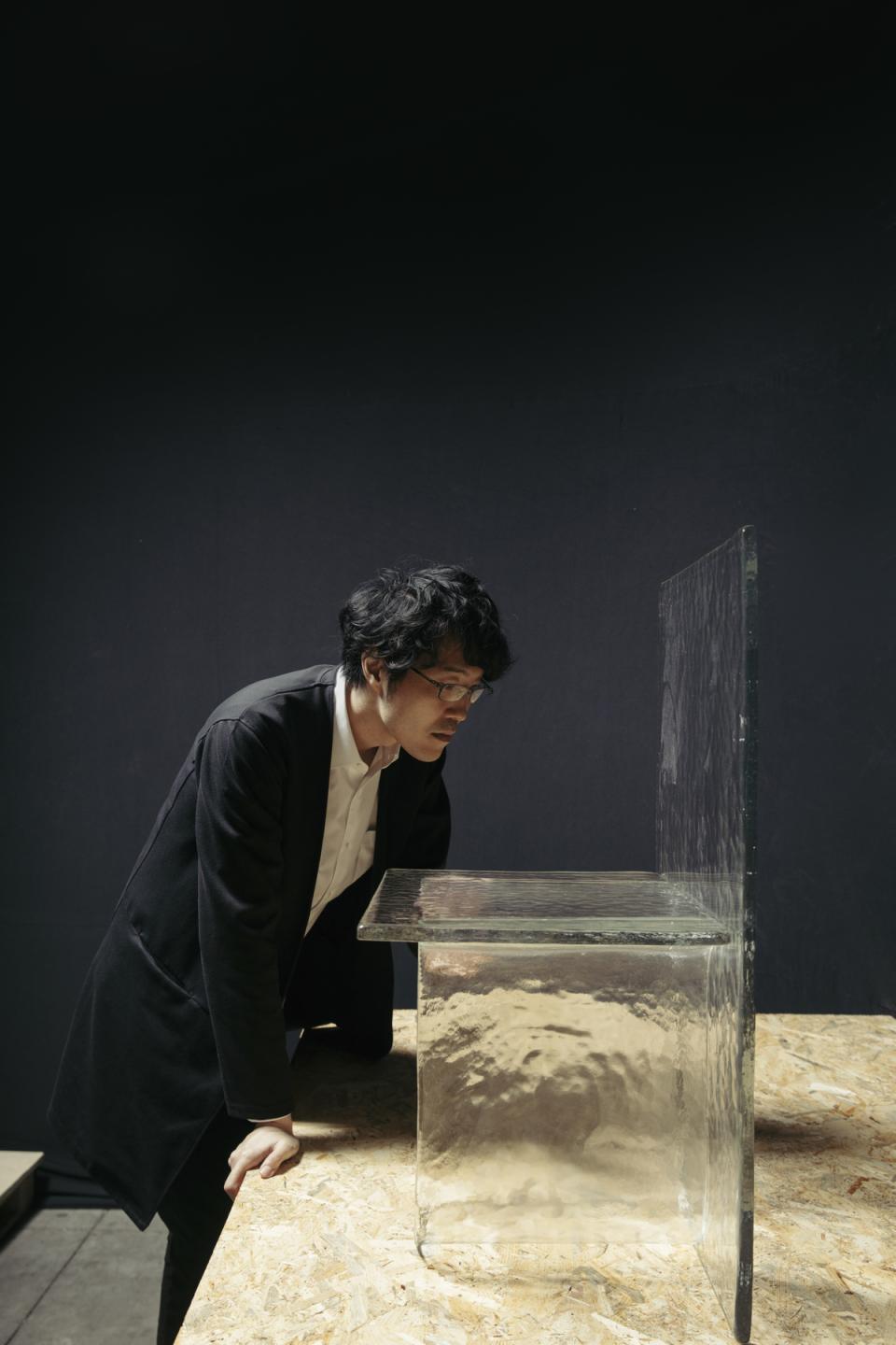 Designer intently examines Melt, a delicate, cast glass table that appears to float, showcasing innovative furniture design by nendo and WonderGlass.