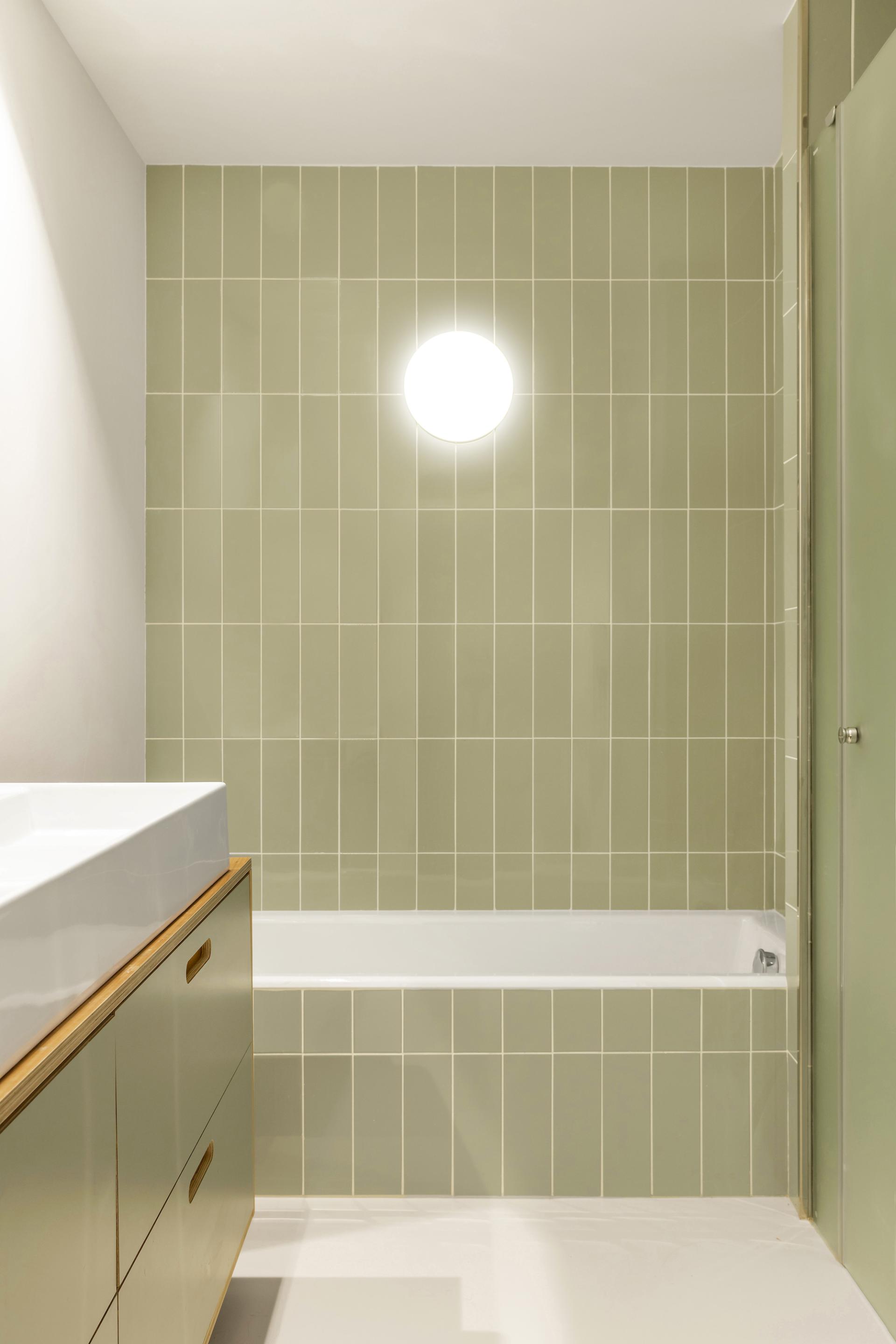 Modern bathroom featuring green ceramic tiles, minimalist wooden cabinetry, and soft lighting, highlighting Spanish ceramic design.