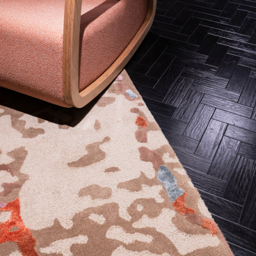 Bespoke rug with organic patterns in earthy tones, complementing modern furniture on a dark herringbone floor.