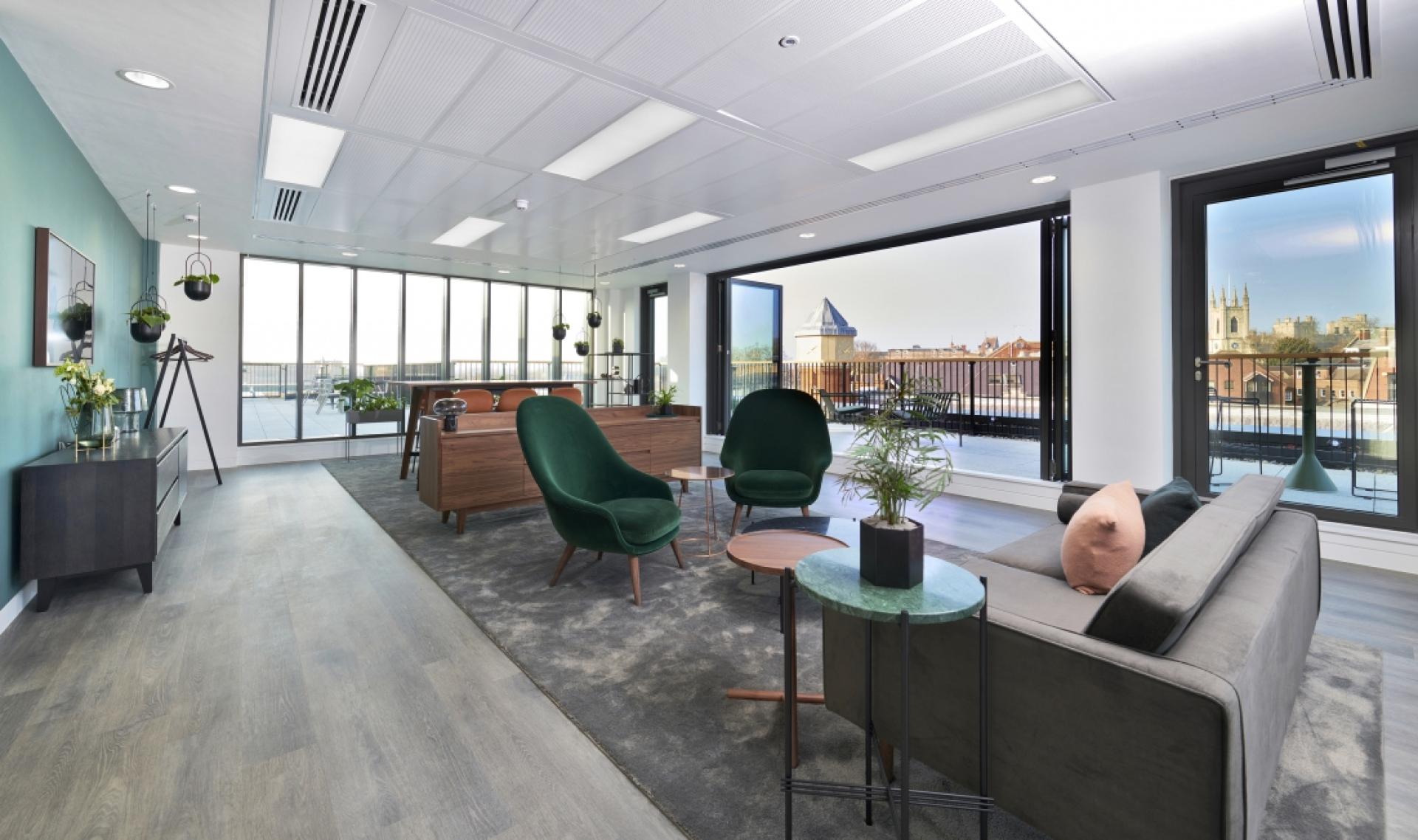 Modern office interior featuring stylish green chairs, a comfortable sofa, and large windows offering a city view.