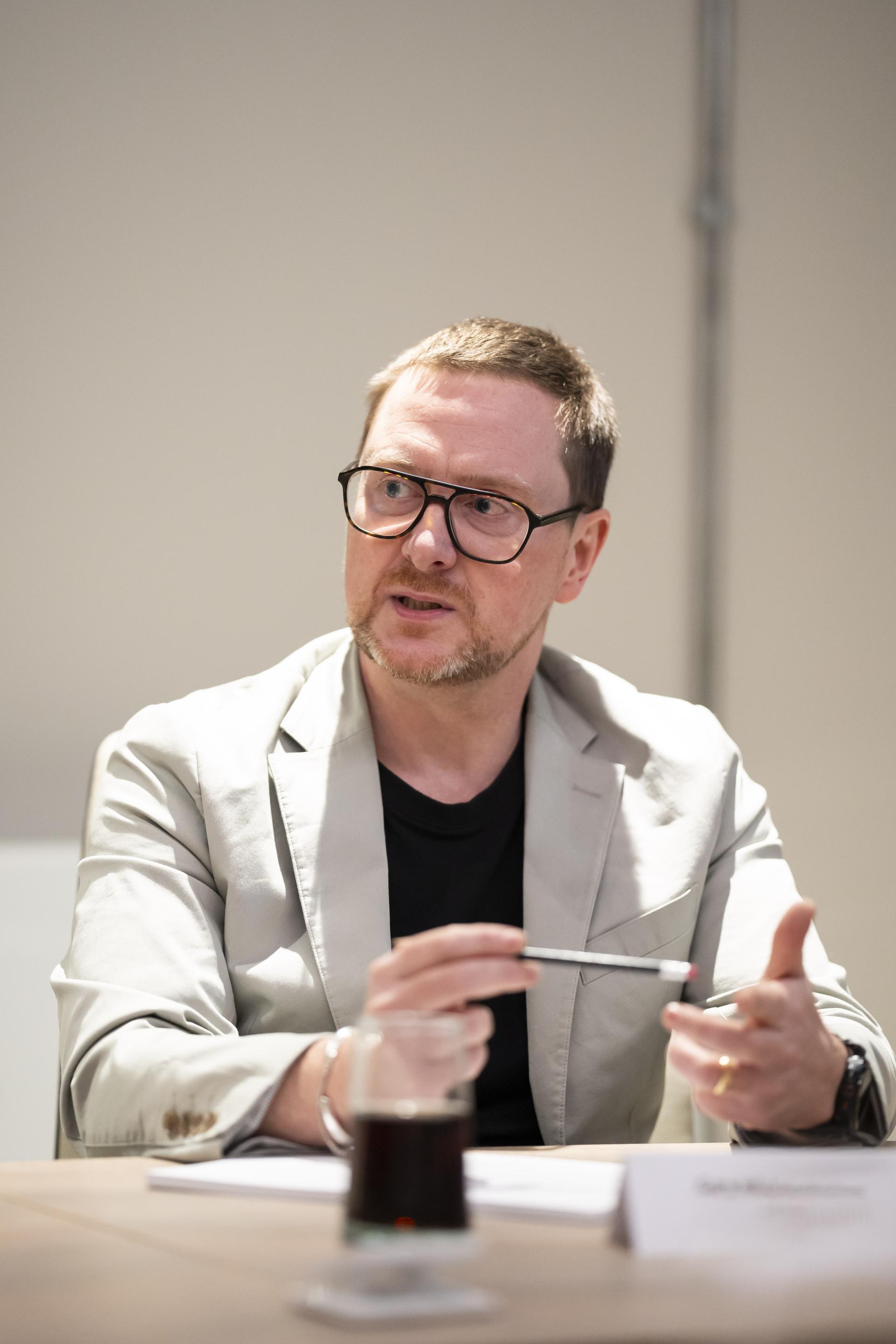 Senior professional discussing sustainable design technology, holding a pen and engaged in conversation at a meeting table.
