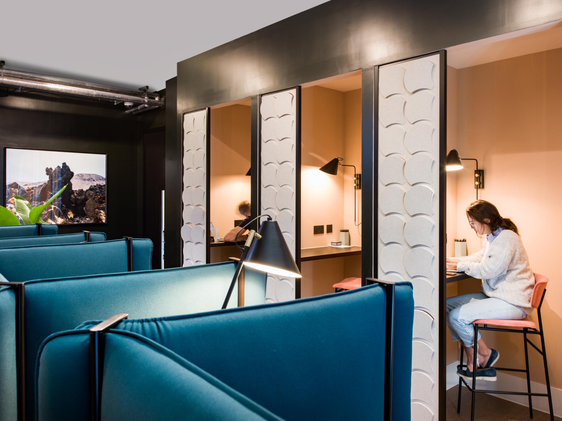 Modern workspace featuring flexible seating areas, private study pods, and a young woman working at a desk, enhancing productivity.