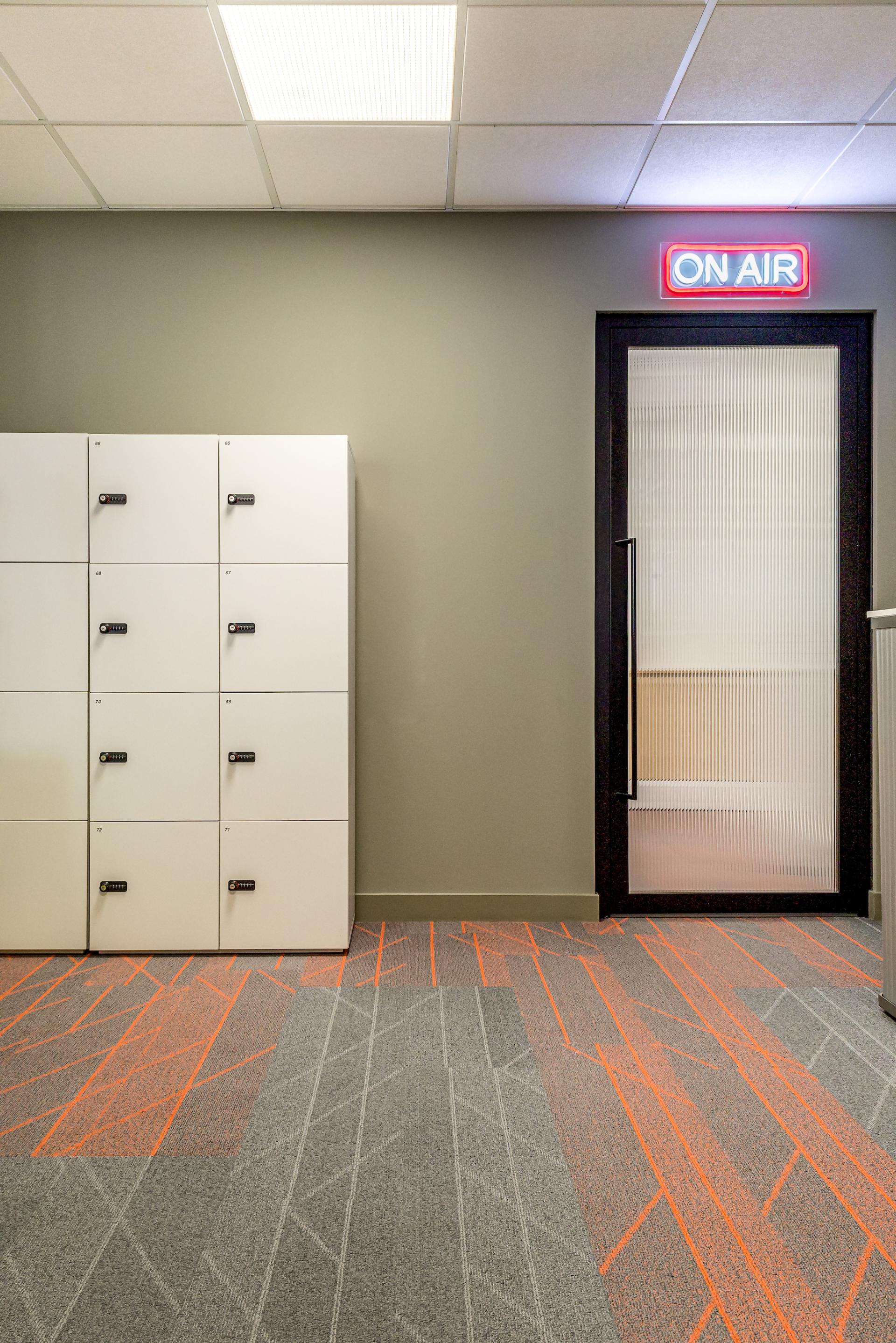 Modern office hallway featuring storage lockers, vibrant carpet design, and an illuminated "ON AIR" sign.