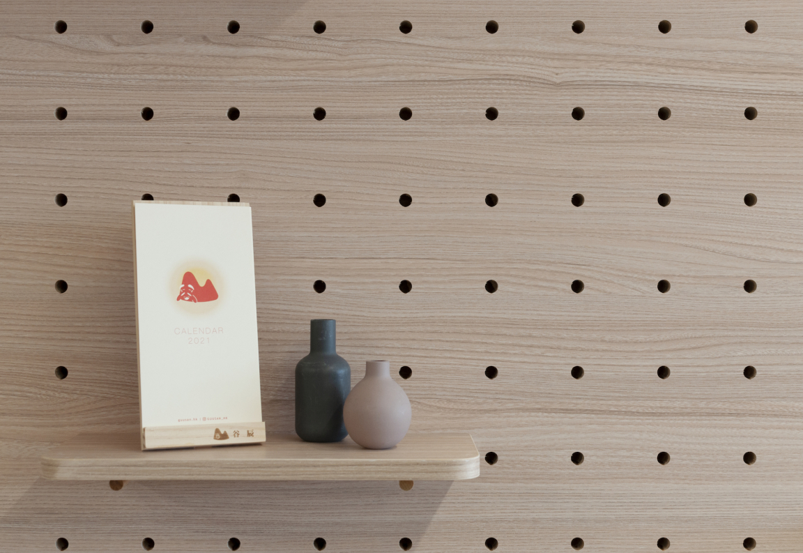 Minimalist display of a 2021 calendar and two ceramic vases on a wooden shelf with a pegboard background.