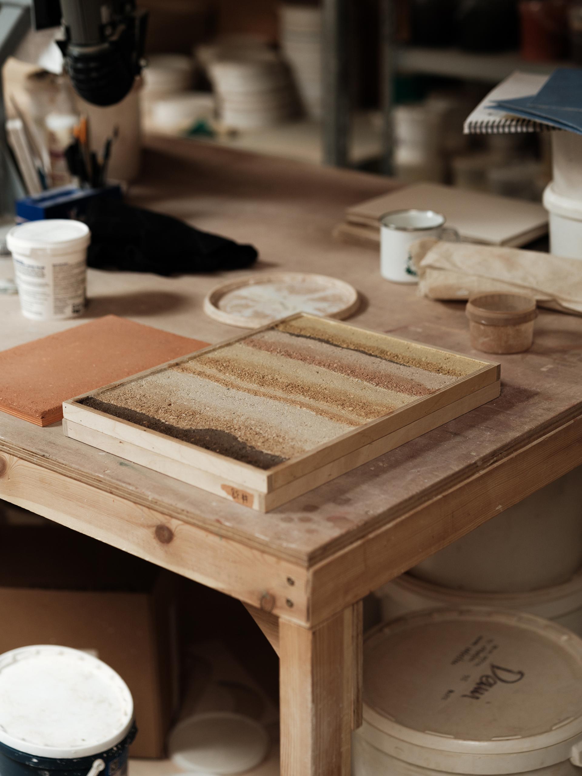 Samples of natural materials for sustainable wall finishes on a wooden table in a workshop.