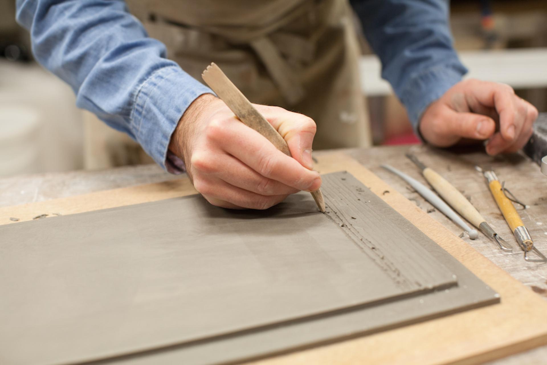 Ceramic artist Matthew Raw carves intricate designs into clay slabs using sculpting tools in his studio.